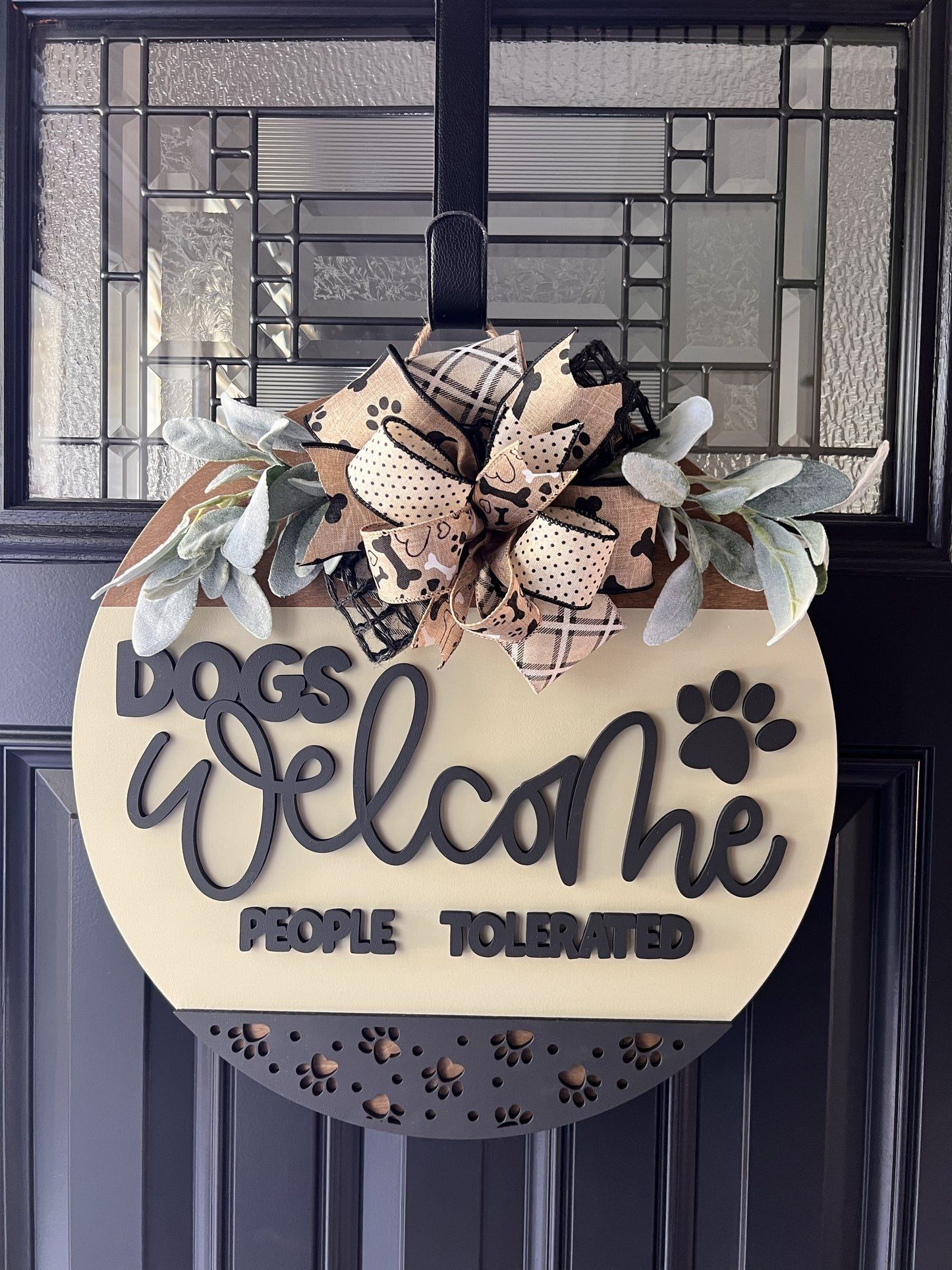 “Dogs Welcome People Tolerated wooden door hanger with layered lettering, paw print accents and decorative bow on front door”
