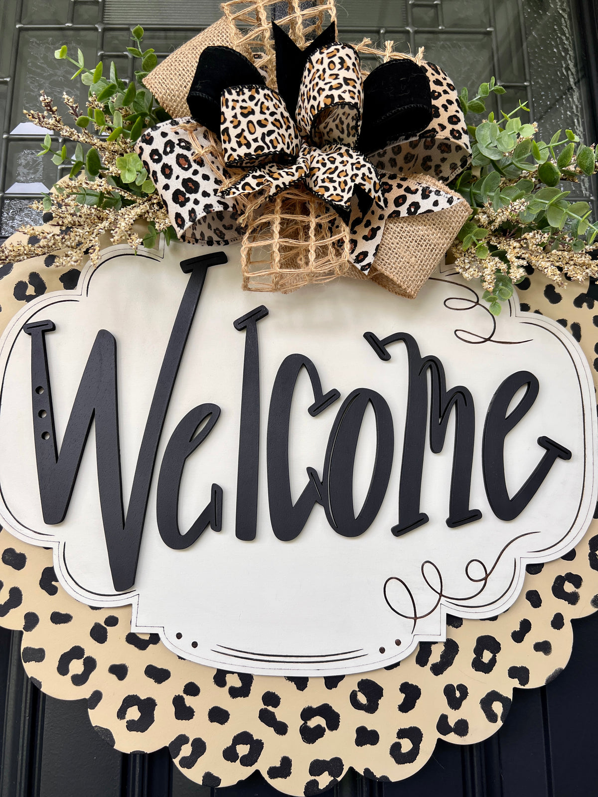 Full view of leopard scalloped Welcome door hanger hanging on black paneled door