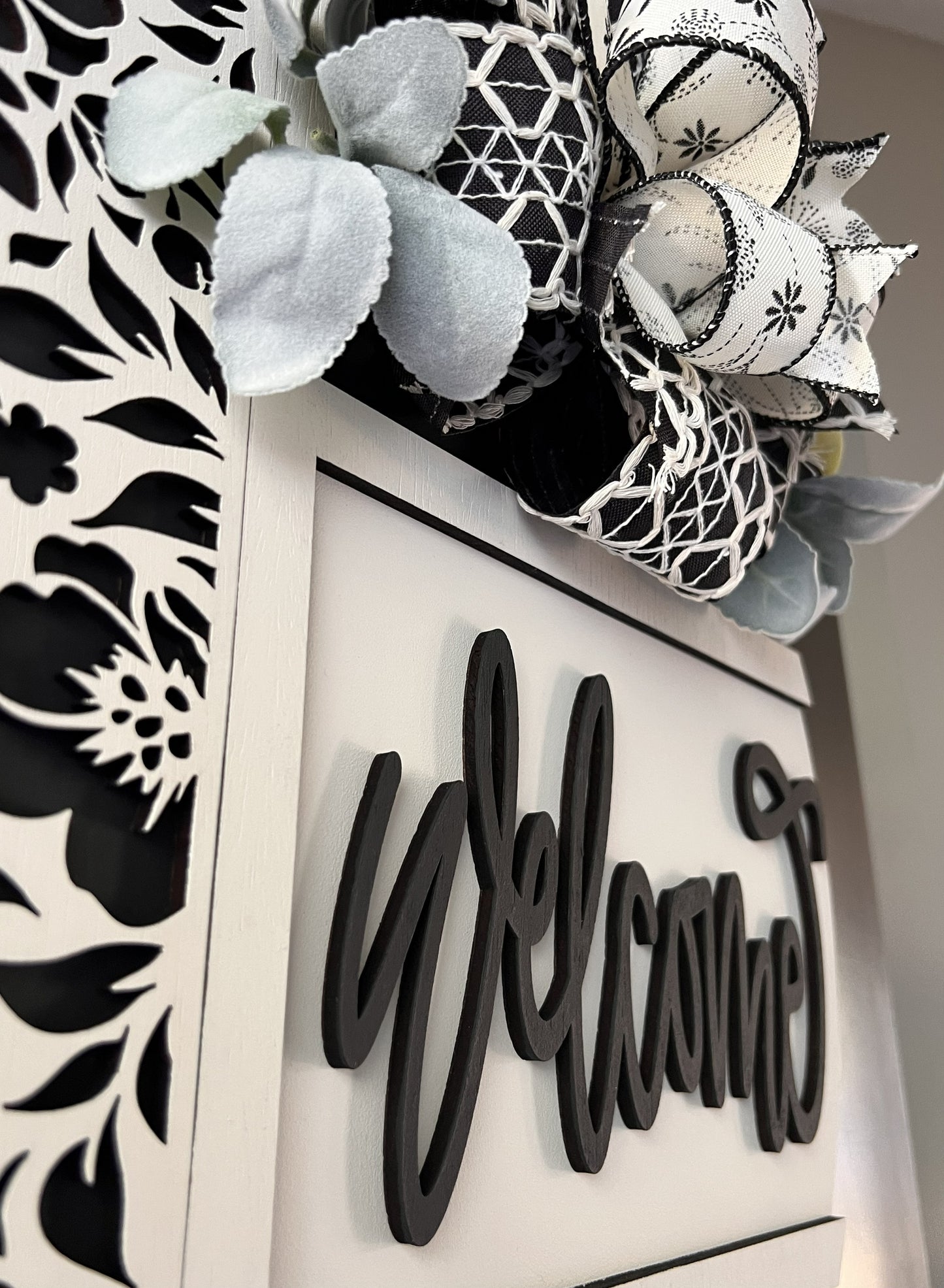 Decorative birchwood wreath with floral and geometric patterns on a 'Welcome' sign.