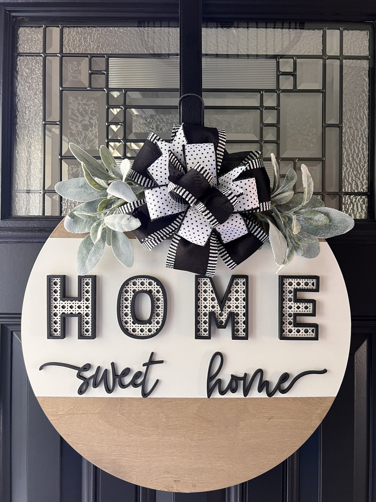 “Home Sweet Home black and white wooden door hanger with layered lettering, decorative bow and greenery on front door”