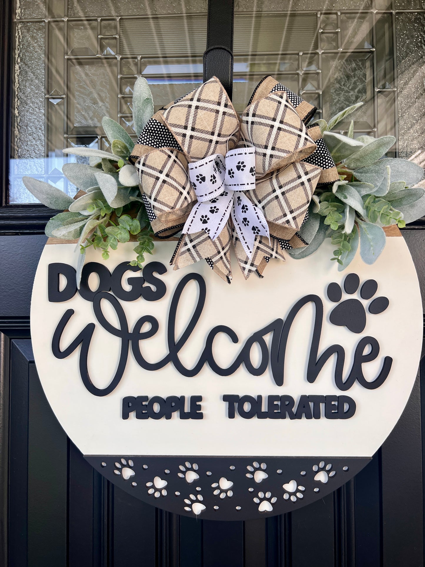 Dogs Welcome People Tolerated door hanger full front view showing complete white round with charcoal paw print border and layered bow