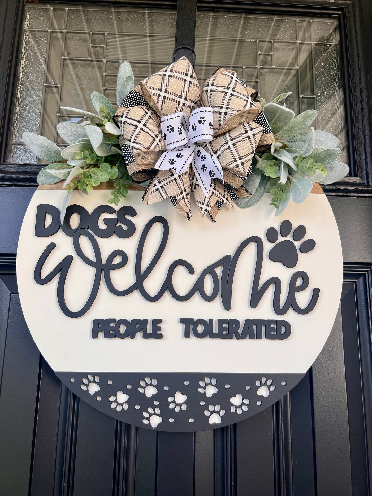 Dogs Welcome People Tolerated door hanger full view on black door showing bow detail with plaid and paw print ribbons and lambs ear sprays