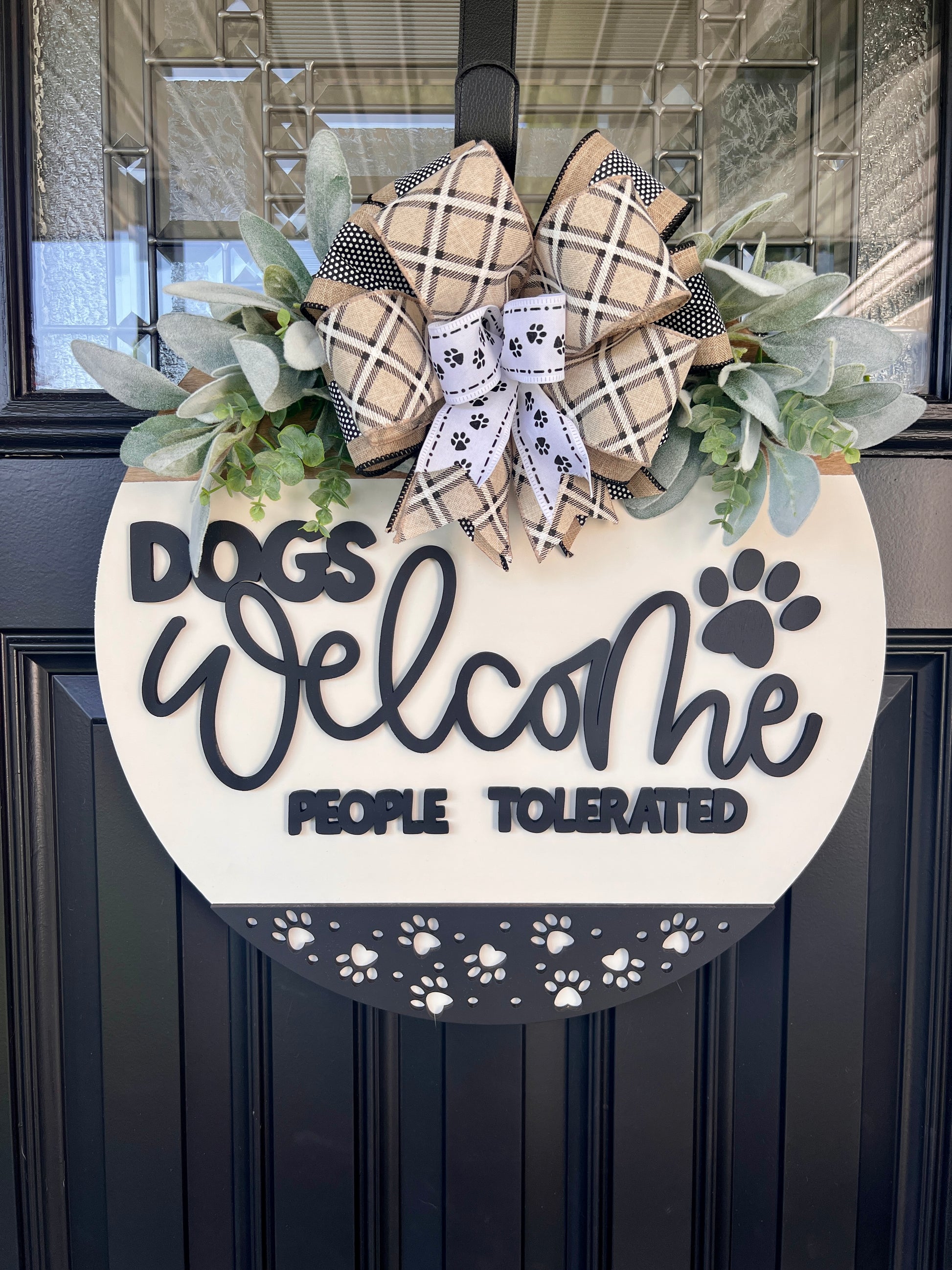 Dogs Welcome People Tolerated door hanger full view on black front door with plaid burlap and paw print bow and eucalyptus greenery