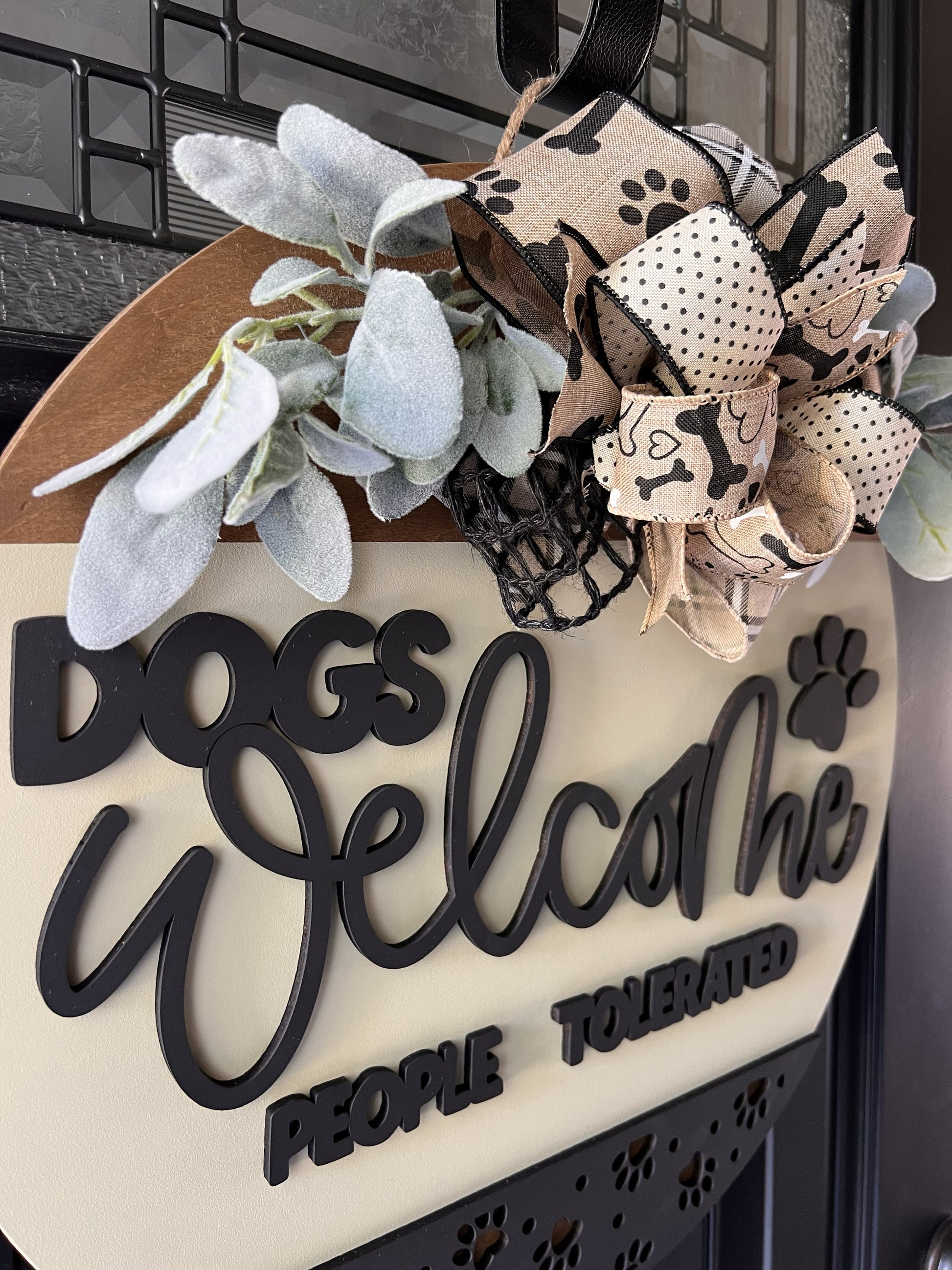 Decorative sign with 'Dogs Welcome, People Tolerated' text with bow and greenery. 