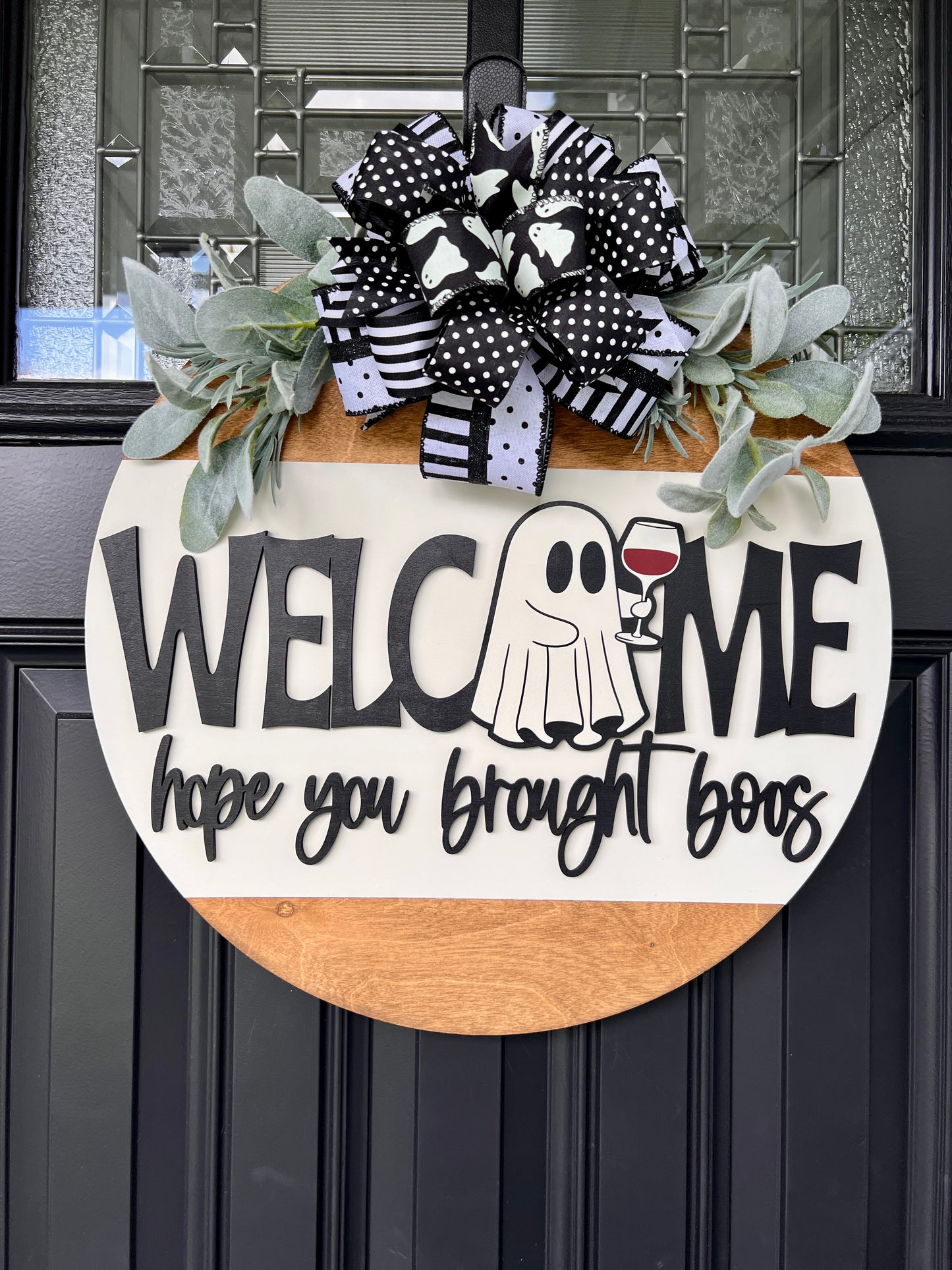Welcome Hope You Brought Boos Halloween door hanger on black front door with ghost wine glass and layered black white bow and lambs ear greenery