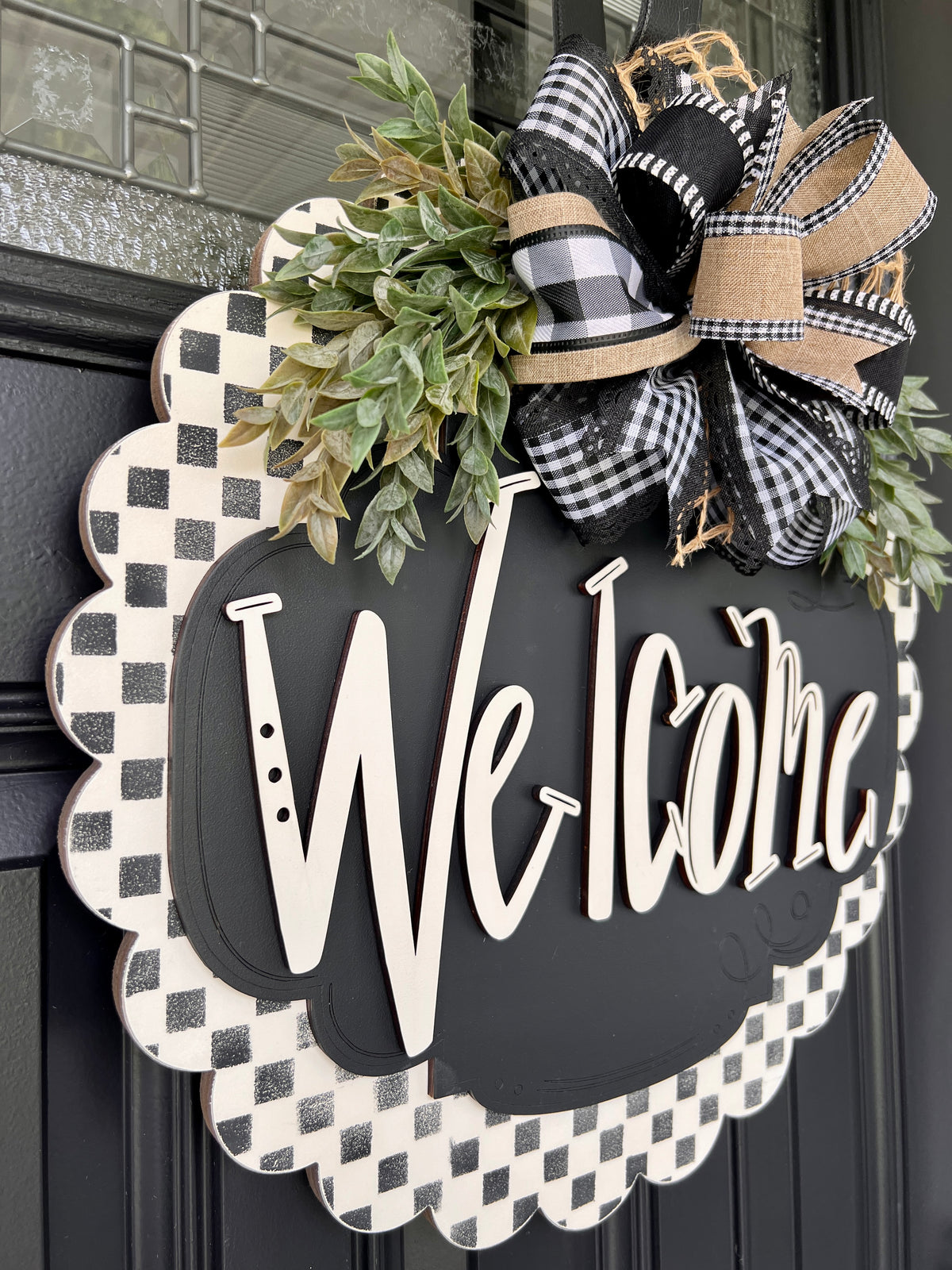 Welcome door hanger with gingham bow hanging on black front door with leaded glass window