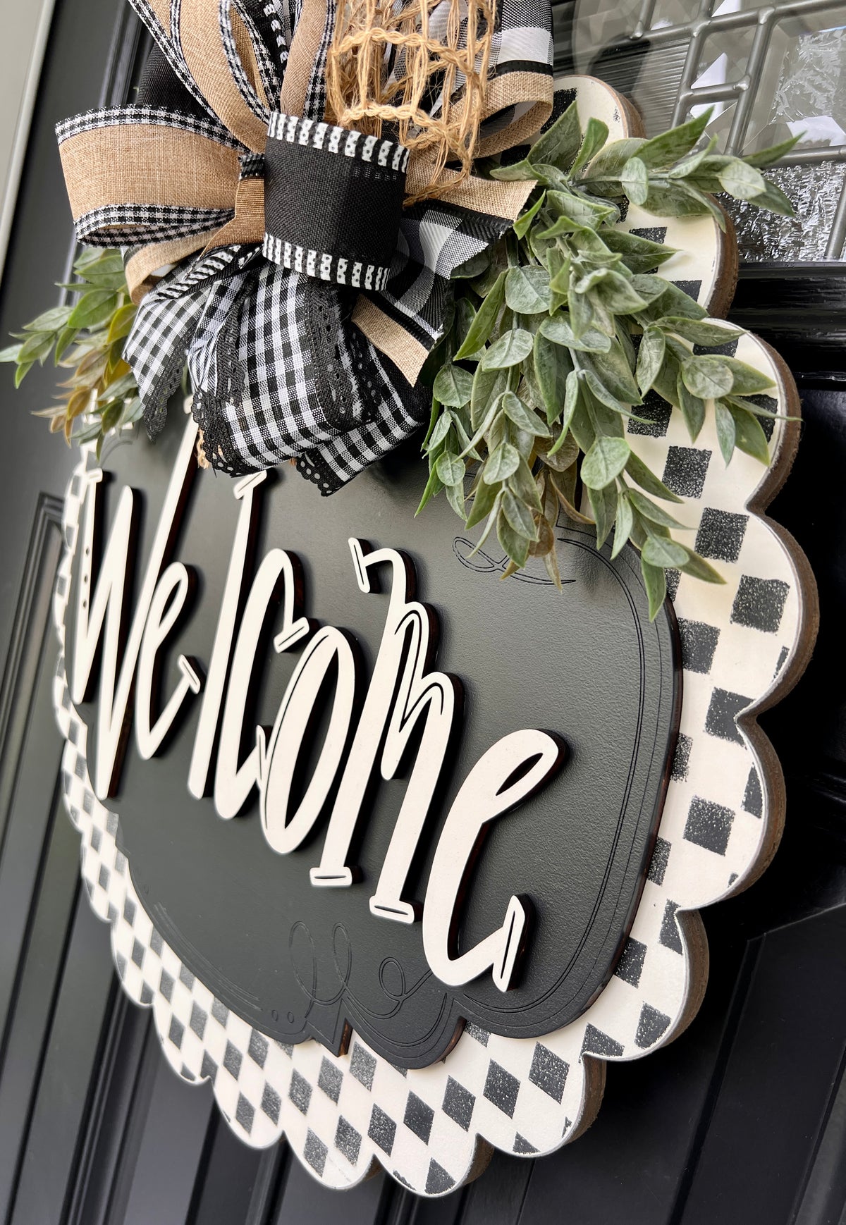 Angled detail of raised cream Welcome letters and glittery black checkered border on wood door sign