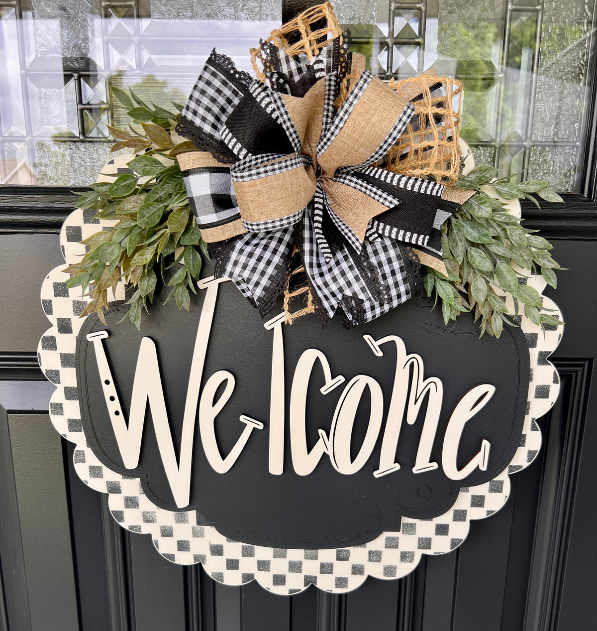 Handmade welcome door hanger with black and white checkered scalloped border and gingham bow hanging on a black front door