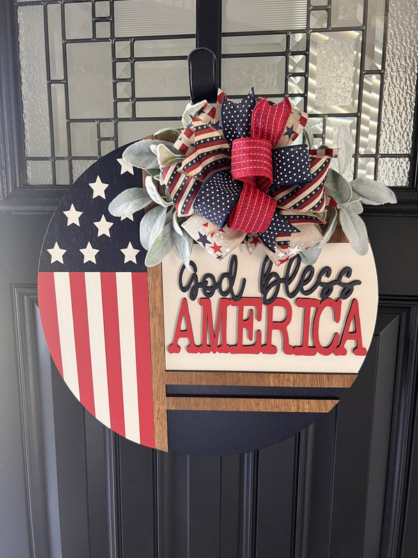 Americana door hanger with American flag design and 'God bless America' text on a black door.