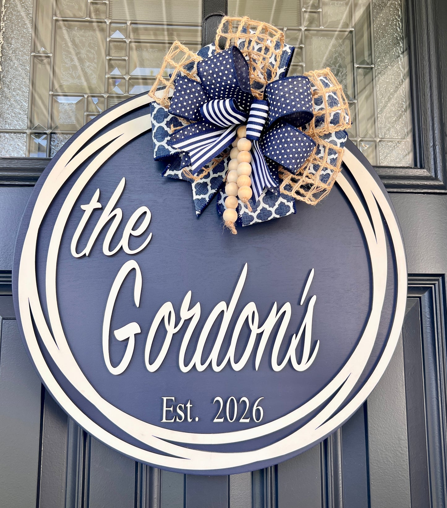 Custom family name door hanger full front view showing the Gordons Est 2026 with layered navy quatrefoil polka dot and jute burlap bow
