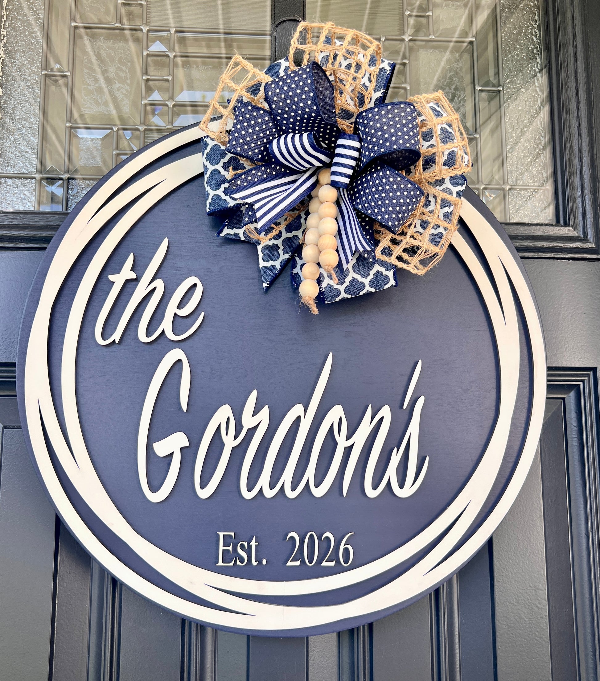 Custom family name door hanger full front view showing the Gordons Est 2026 with layered navy quatrefoil polka dot and jute burlap bow