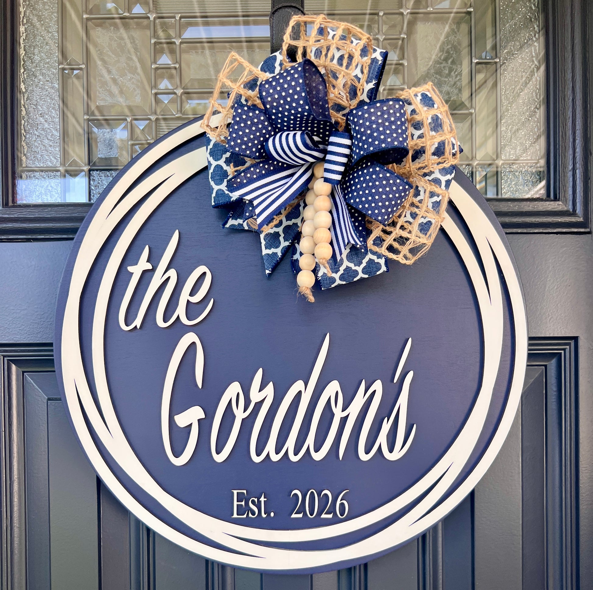 Custom family name door hanger showing the Gordons Est 2026 on navy blue 18 inch round with cream circle frame and layered navy bow