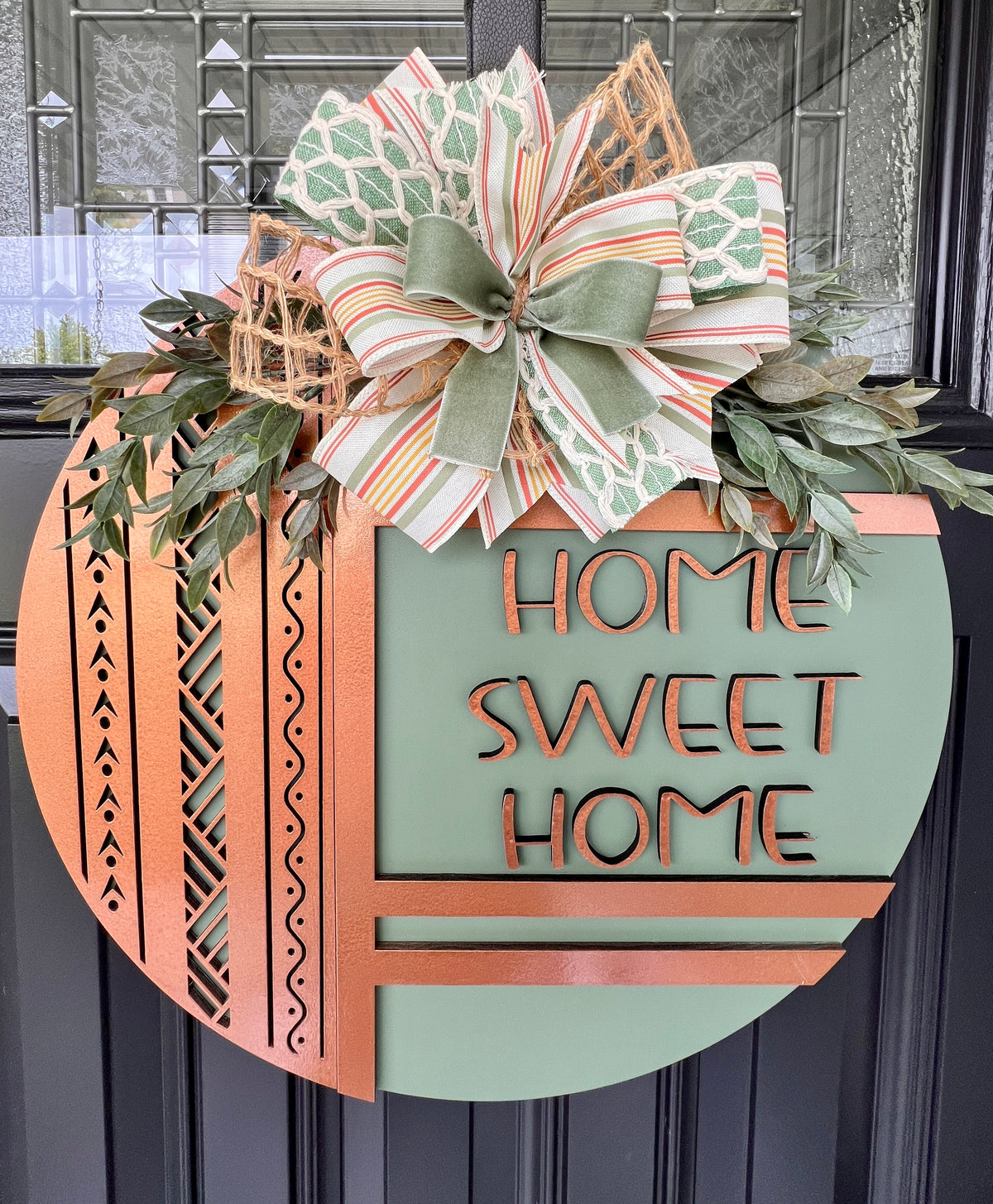 Sage green Home Sweet Home wood door hanger with warm copper frame details, faux greenery, and striped sage and natural ribbon bow