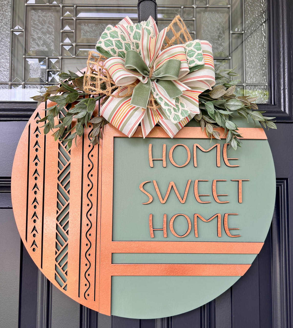 Handmade sage green and copper Home Sweet Home birchwood door hanger with geometric laser-cut details, faux greenery, and layered ribbon bow