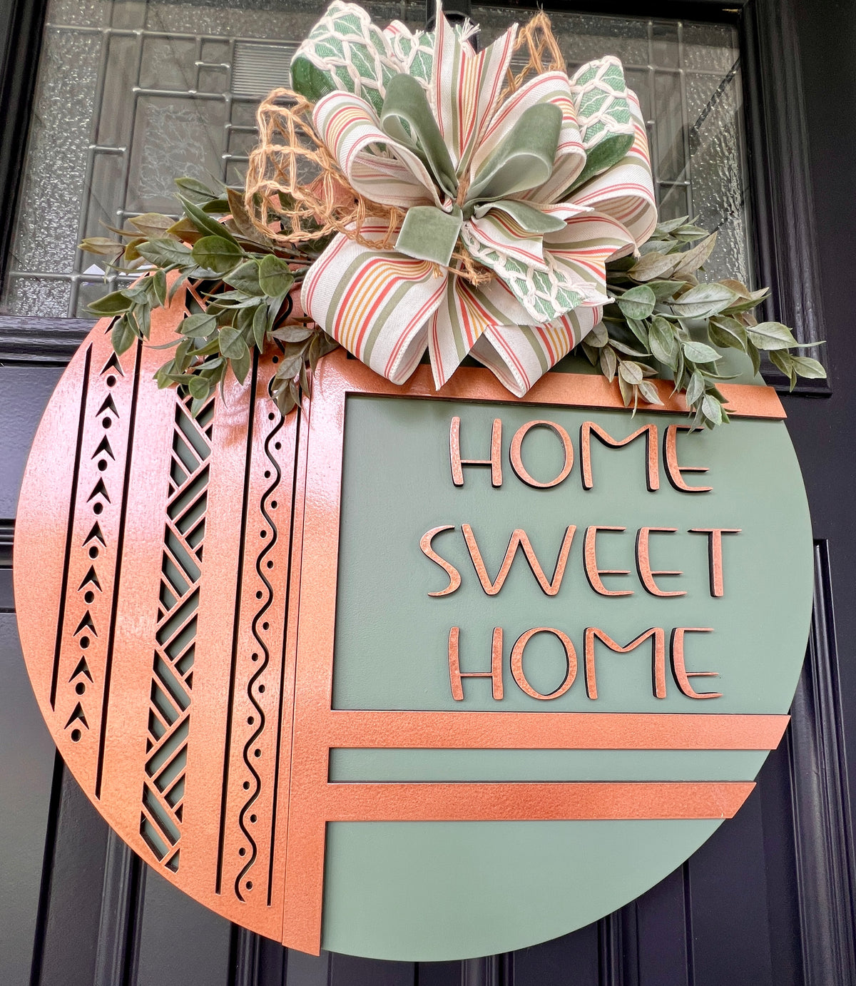 Front view of sage green Home Sweet Home birchwood door hanger with copper accents, laser-cut geometric details, faux greenery, and ribbon bow
