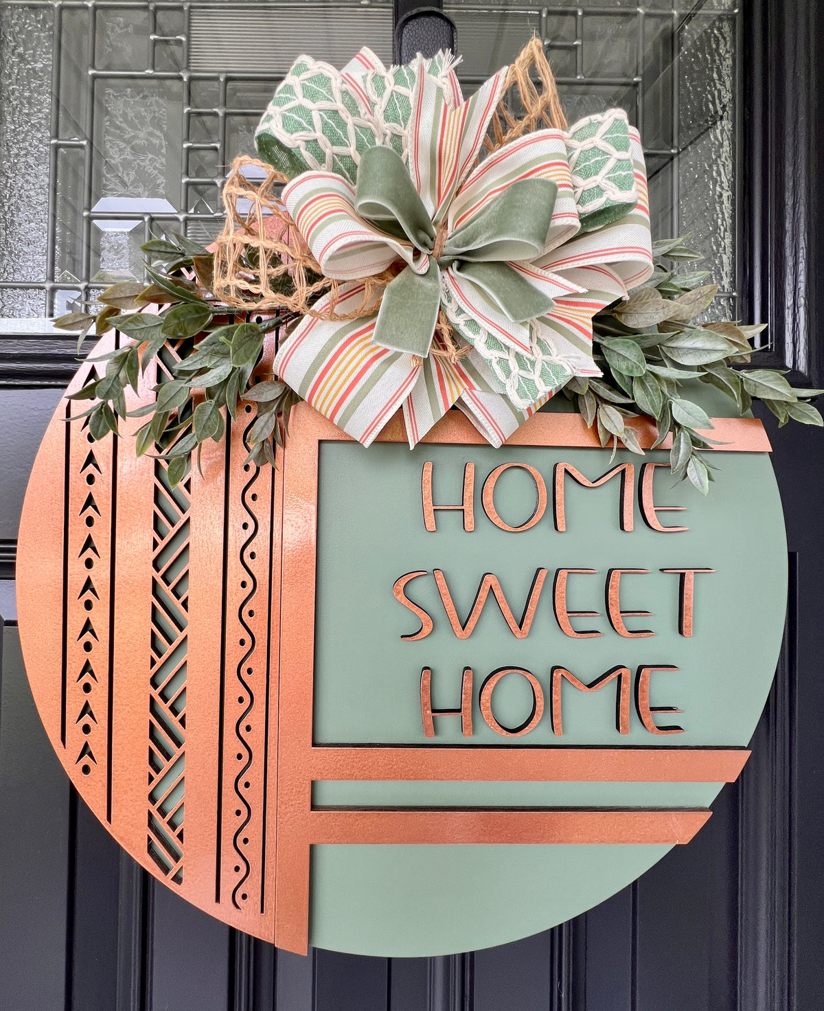 Side view of dimensional Home Sweet Home birchwood door hanger showing raised copper lettering, layered construction, greenery, and ribbon bow