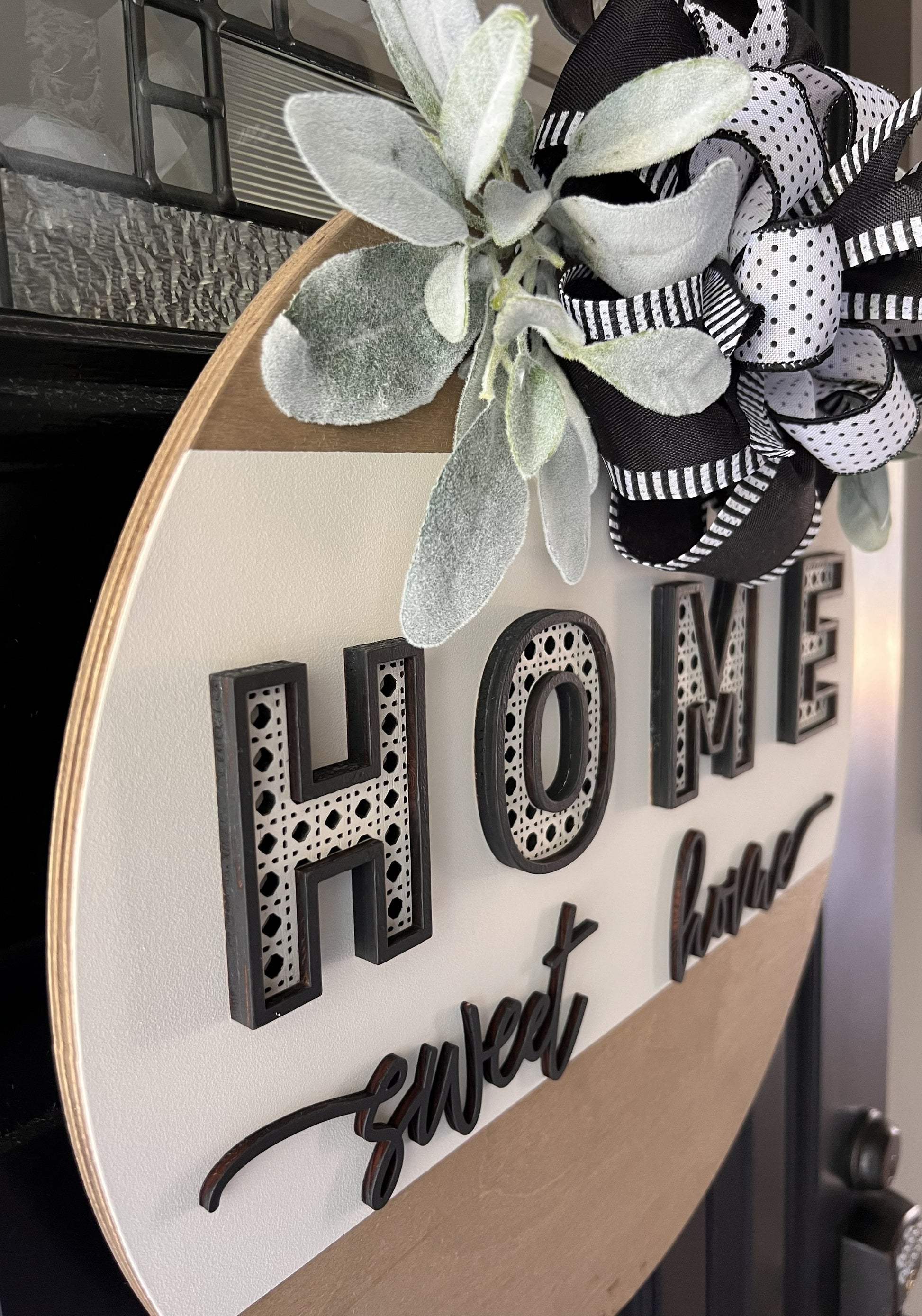 “Home Sweet Home black and white wooden door hanger with layered lettering, decorative bow and greenery on front door”