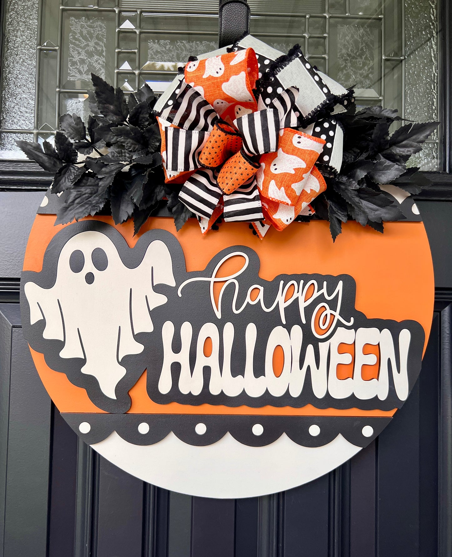 Happy Halloween ghost door hanger close up showing 3D white ghost and charcoal Halloween lettering on orange background