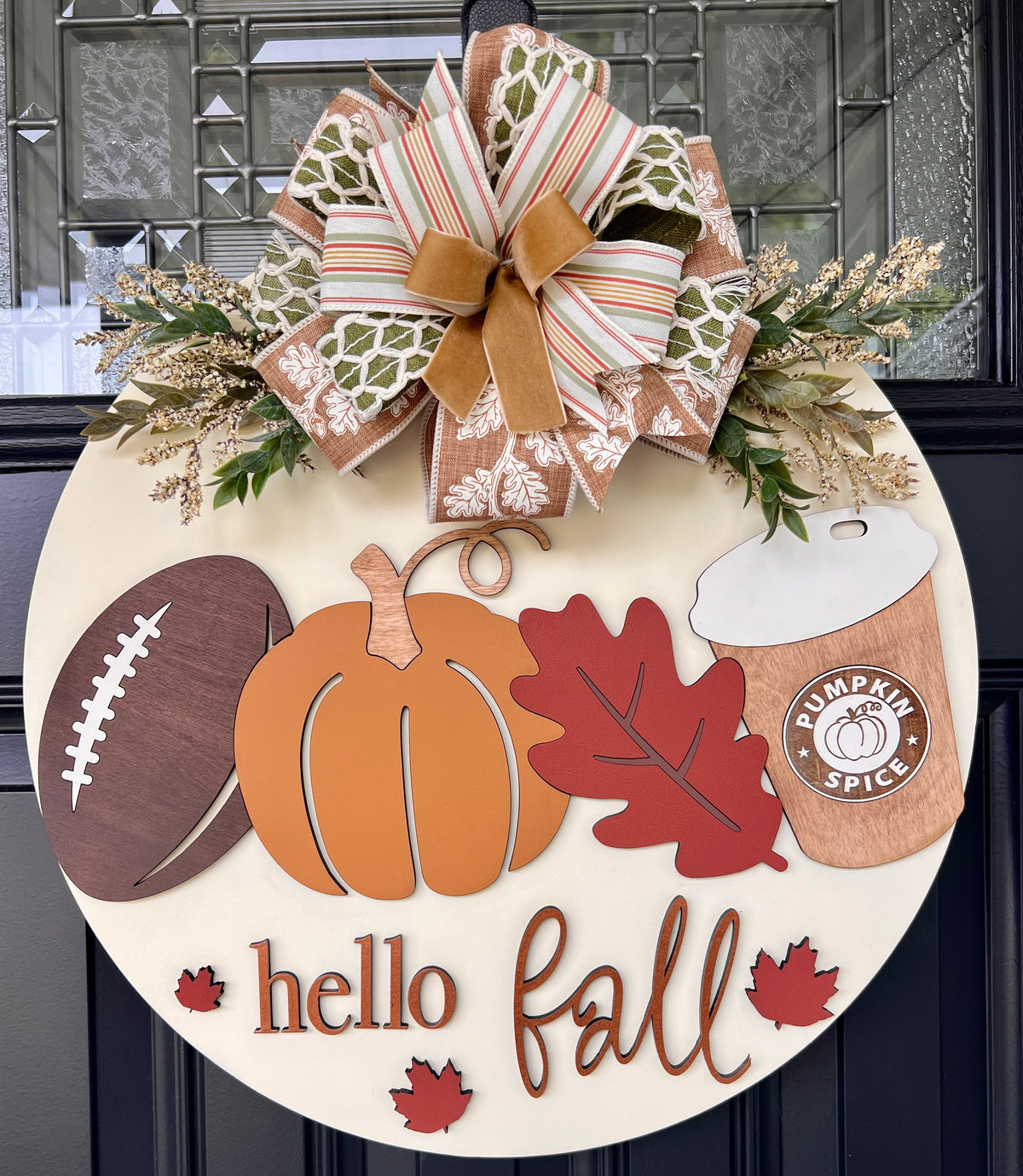Handmade Hello Fall birchwood door hanger with football, pumpkin, red leaf, pumpkin spice cup, greenery, and layered bow on a black front door