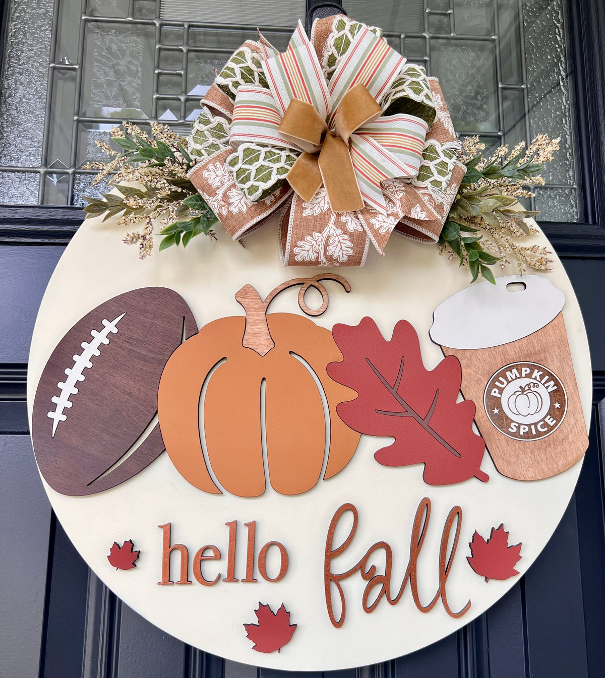 Round Hello Fall door decor made from birchwood with football, pumpkin, fall leaves, pumpkin spice cup, greenery, and neutral striped ribbon bow