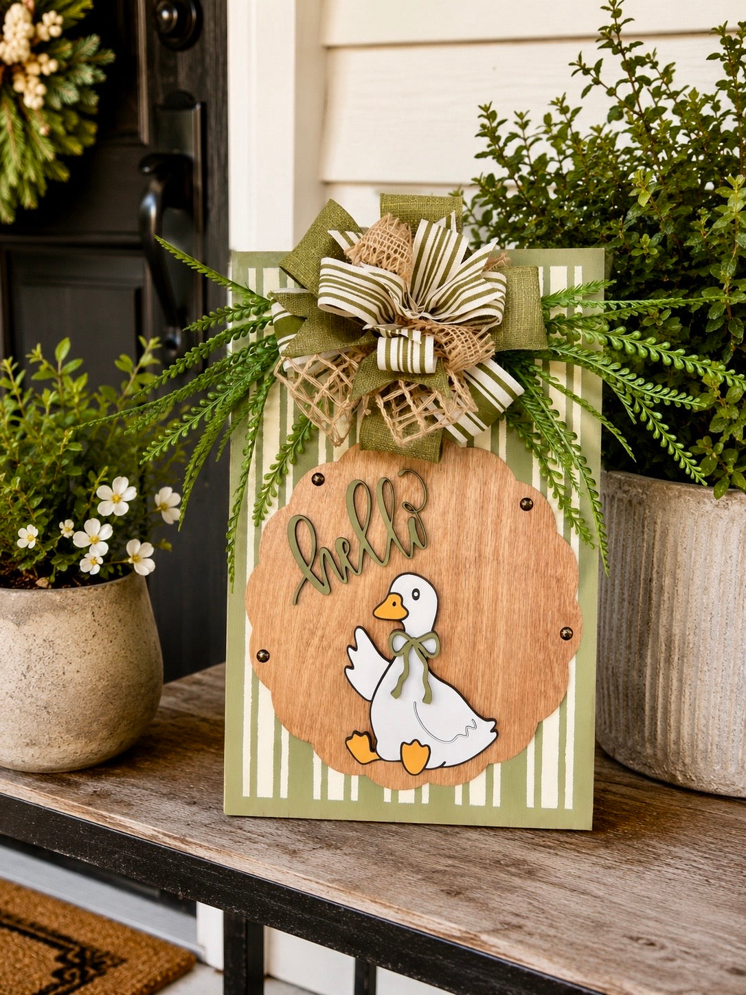 Hello Goose olive green pinstripe door sign styled on porch with greenery and white flowering plants