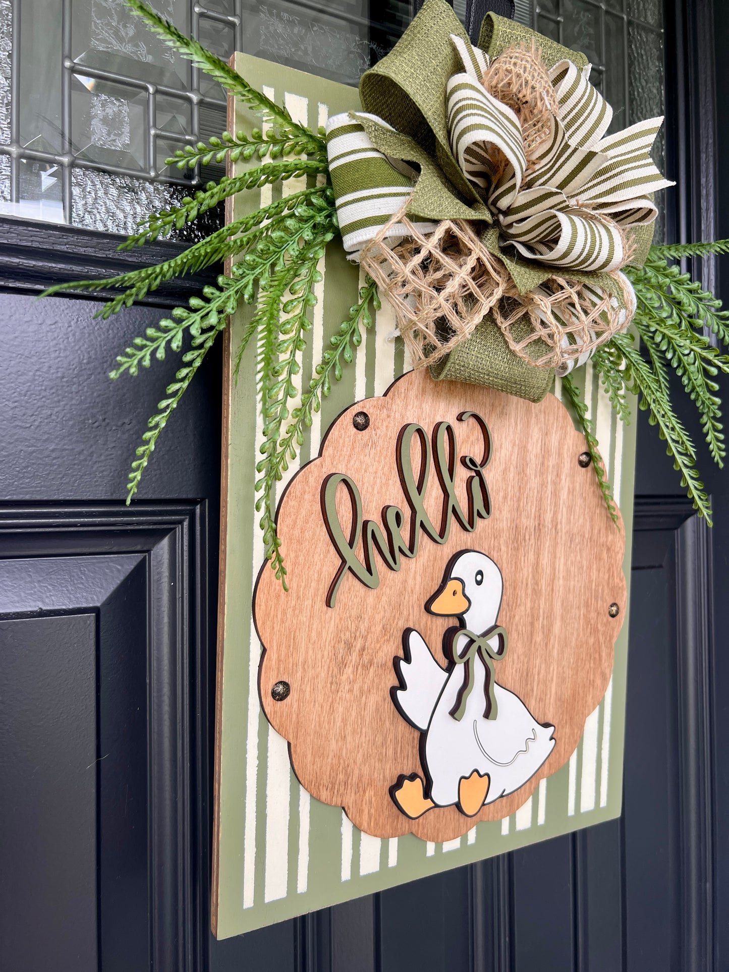 Hello Goose olive green pinstripe door sign on black front door with layered olive burlap and stripe bow and fern greenery