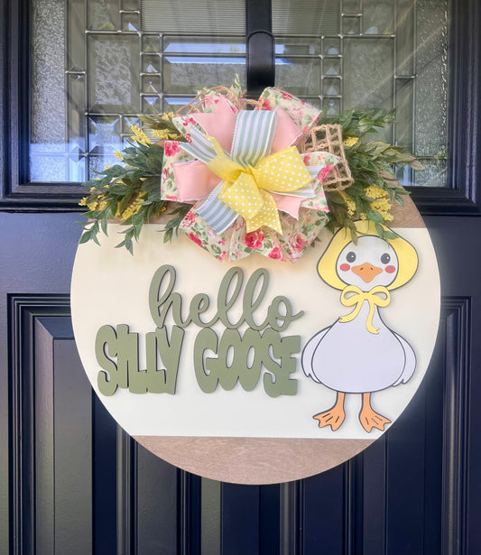 Decorative door hanger with a goose illustration and 'hello silly goose' text on a dark door.