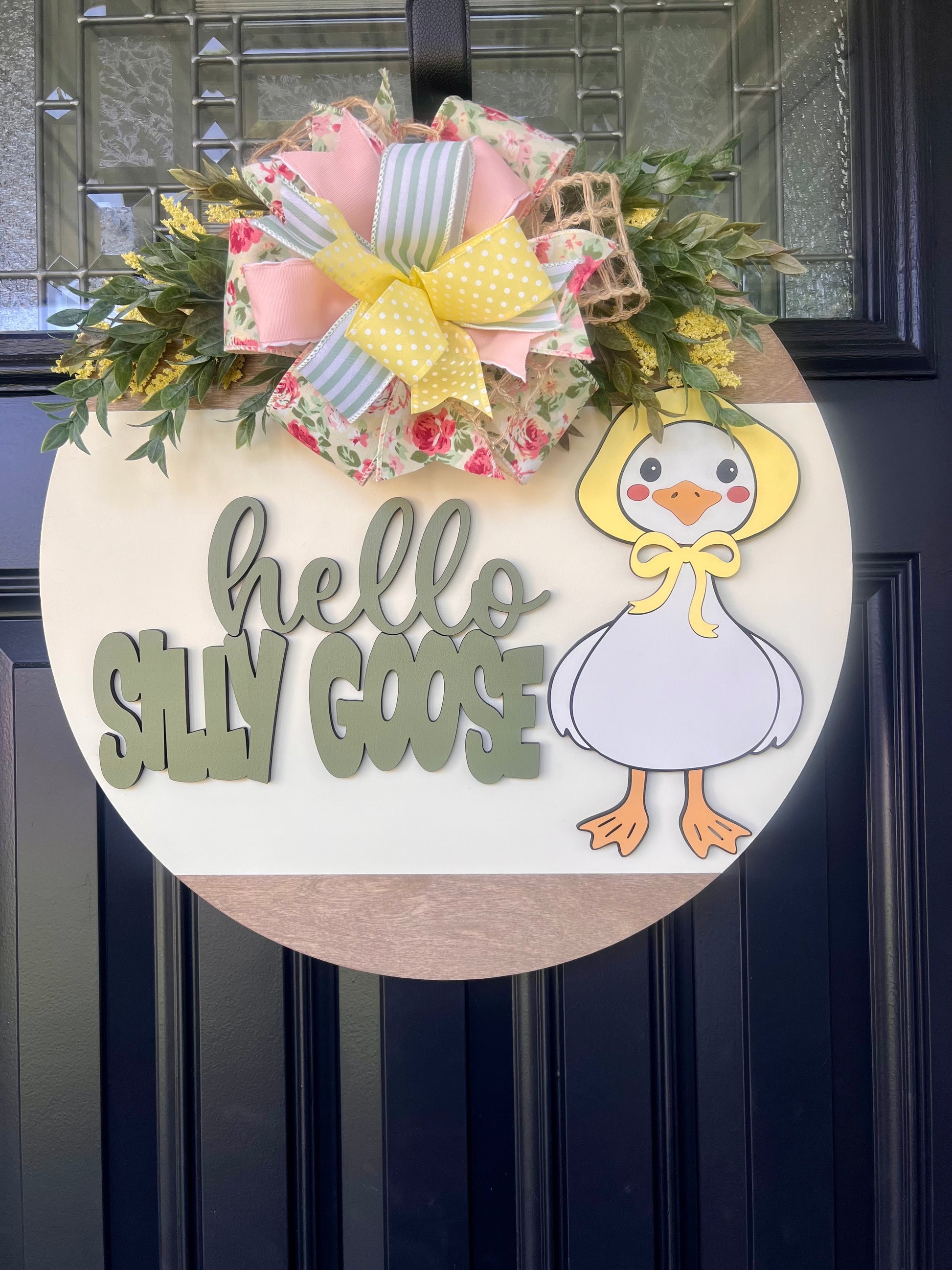 Decorative door hanger with a cartoon goose and colorful bows on a dark surface.