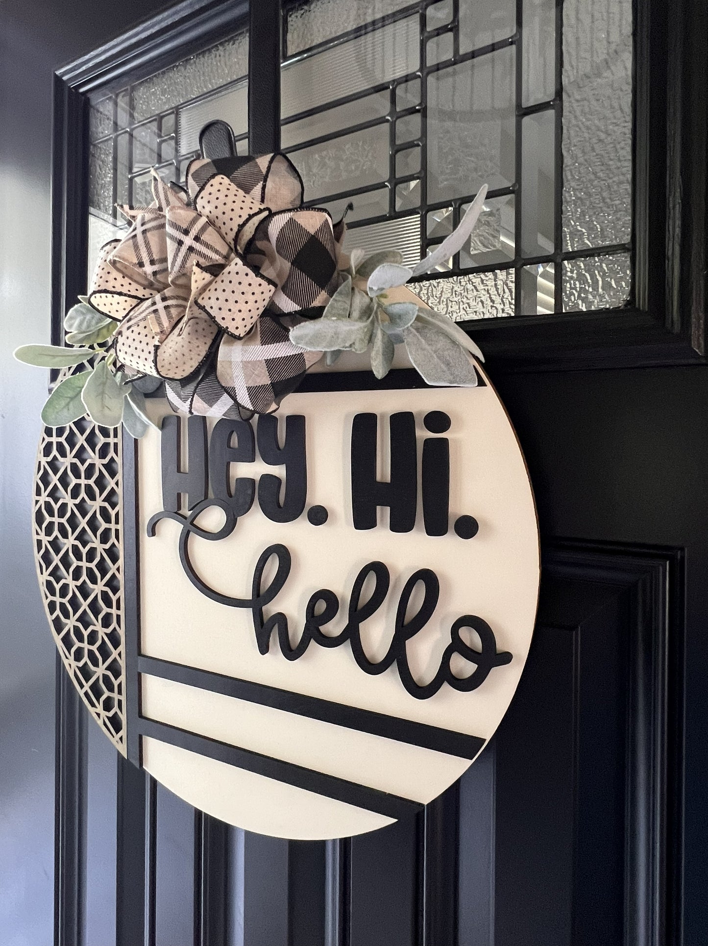 Decorative door hanger with 'Hey. Hi. Hello' text and plaid flowers on a black door.