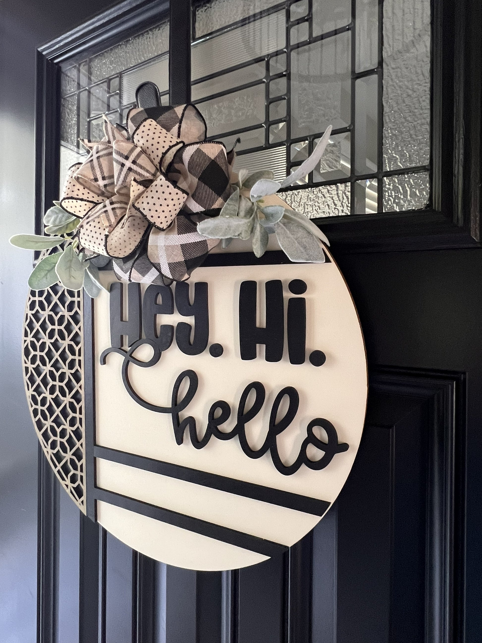 Decorative door hanger with 'Hey. Hi. Hello' text and plaid flowers on a black door.