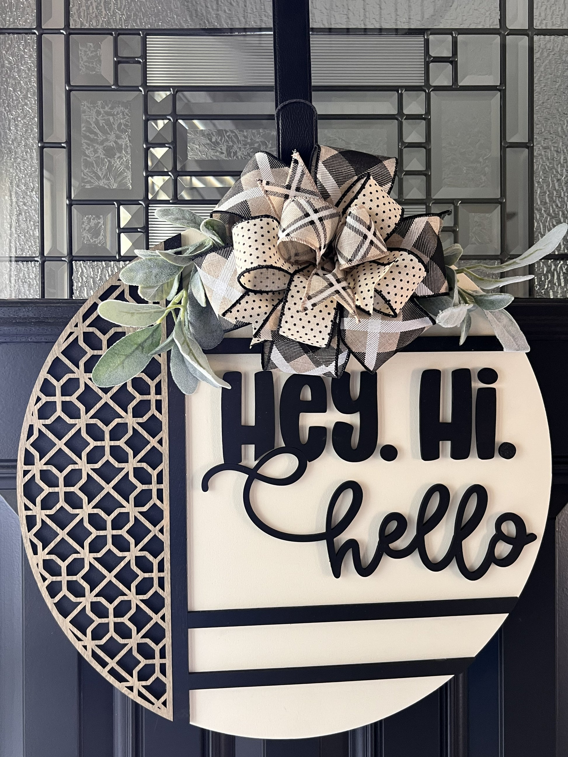 Decorative door hanger with a bow and 'Hey. Hi. Hello' text on a geometric patterned background.