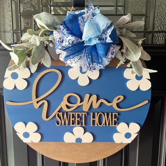 “Blue home sweet home door hanger with raised wooden lettering, floral daisy accents, and designer bow on front door”