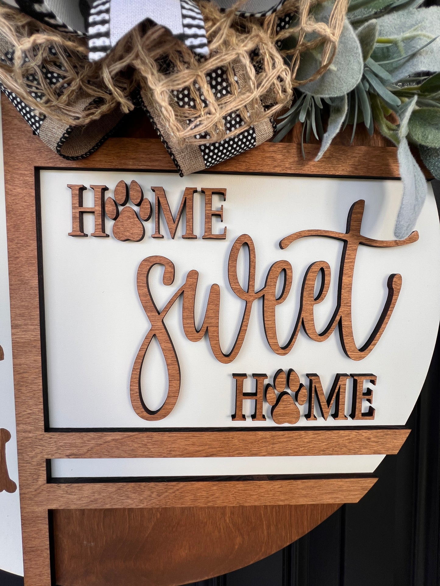 Handmade Home Sweet Home dog lover door hanger featuring laser-cut paw prints, dog bone accents, stained birchwood details, greenery, and a coordinating designer bow.
