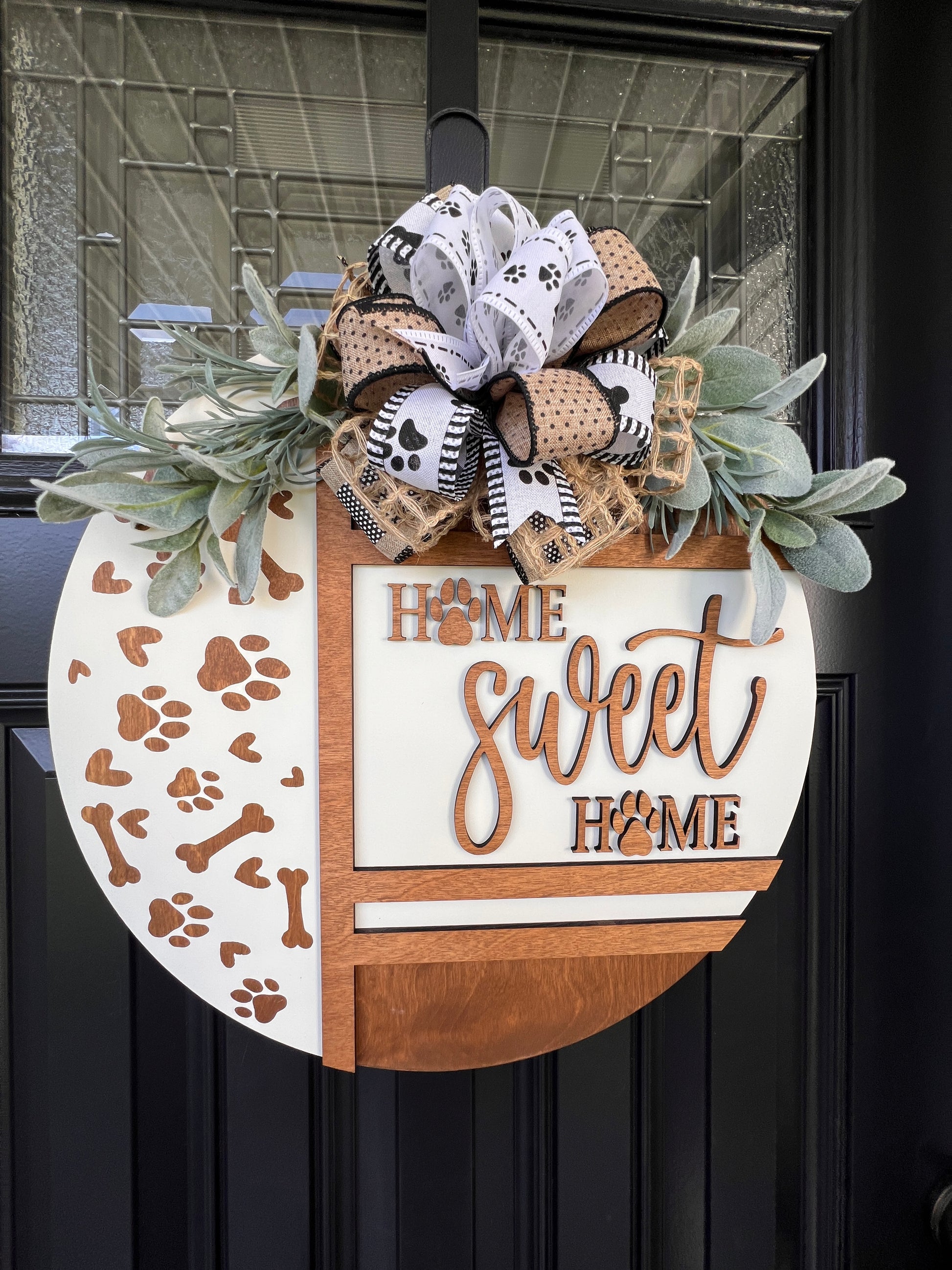 Handmade Home Sweet Home dog lover door hanger featuring laser-cut paw prints, dog bone accents, stained birchwood details, greenery, and a coordinating designer bow.
