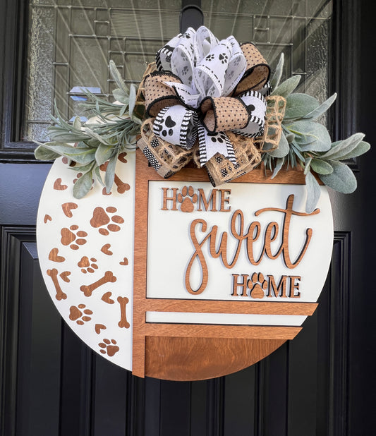 Handmade Home Sweet Home dog lover door hanger featuring laser-cut paw prints, dog bone accents, stained birchwood details, greenery, and a coordinating designer bow.


