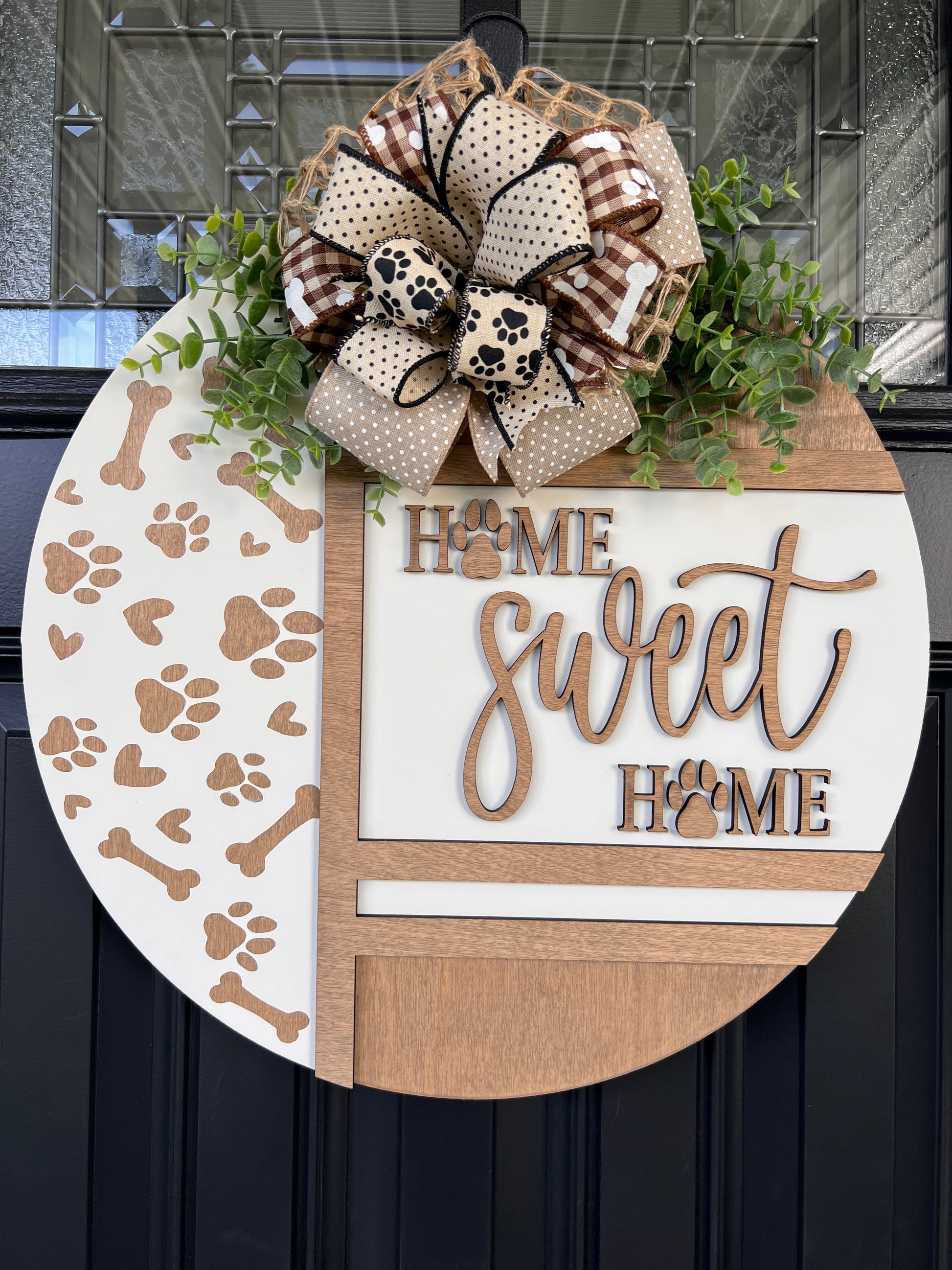 Handmade Home Sweet Home dog lover door hanger featuring laser-cut paw prints, dog bone accents, stained birchwood details, greenery, and a coordinating designer bow. 