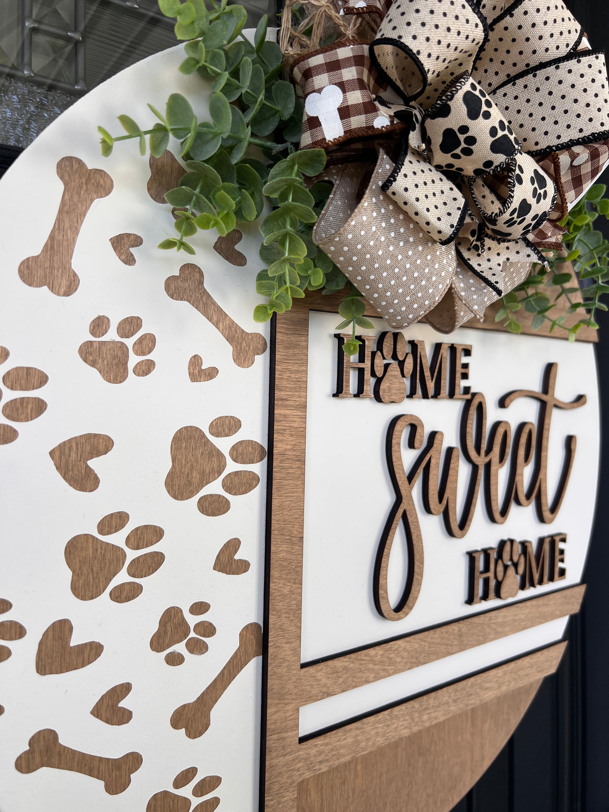 Handmade Home Sweet Home dog lover door hanger featuring laser-cut paw prints, dog bone accents, stained birchwood details, greenery, and a coordinating designer bow. 