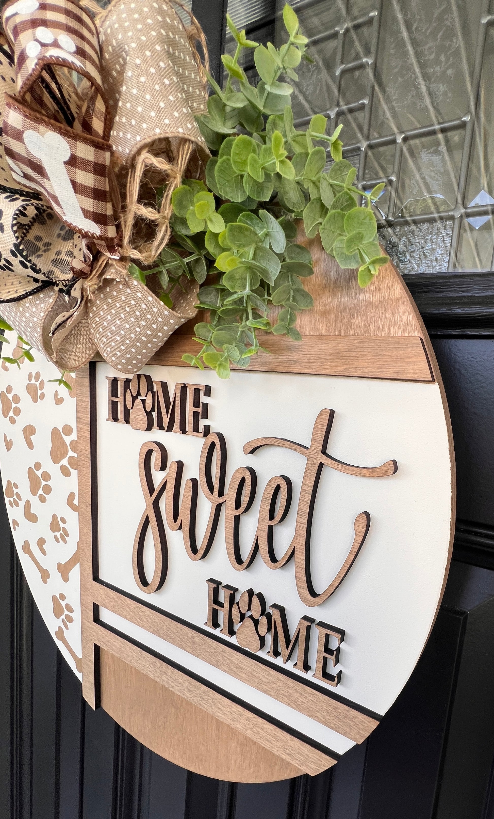 Handmade Home Sweet Home dog lover door hanger featuring laser-cut paw prints, dog bone accents, stained birchwood details, greenery, and a coordinating designer bow. 
