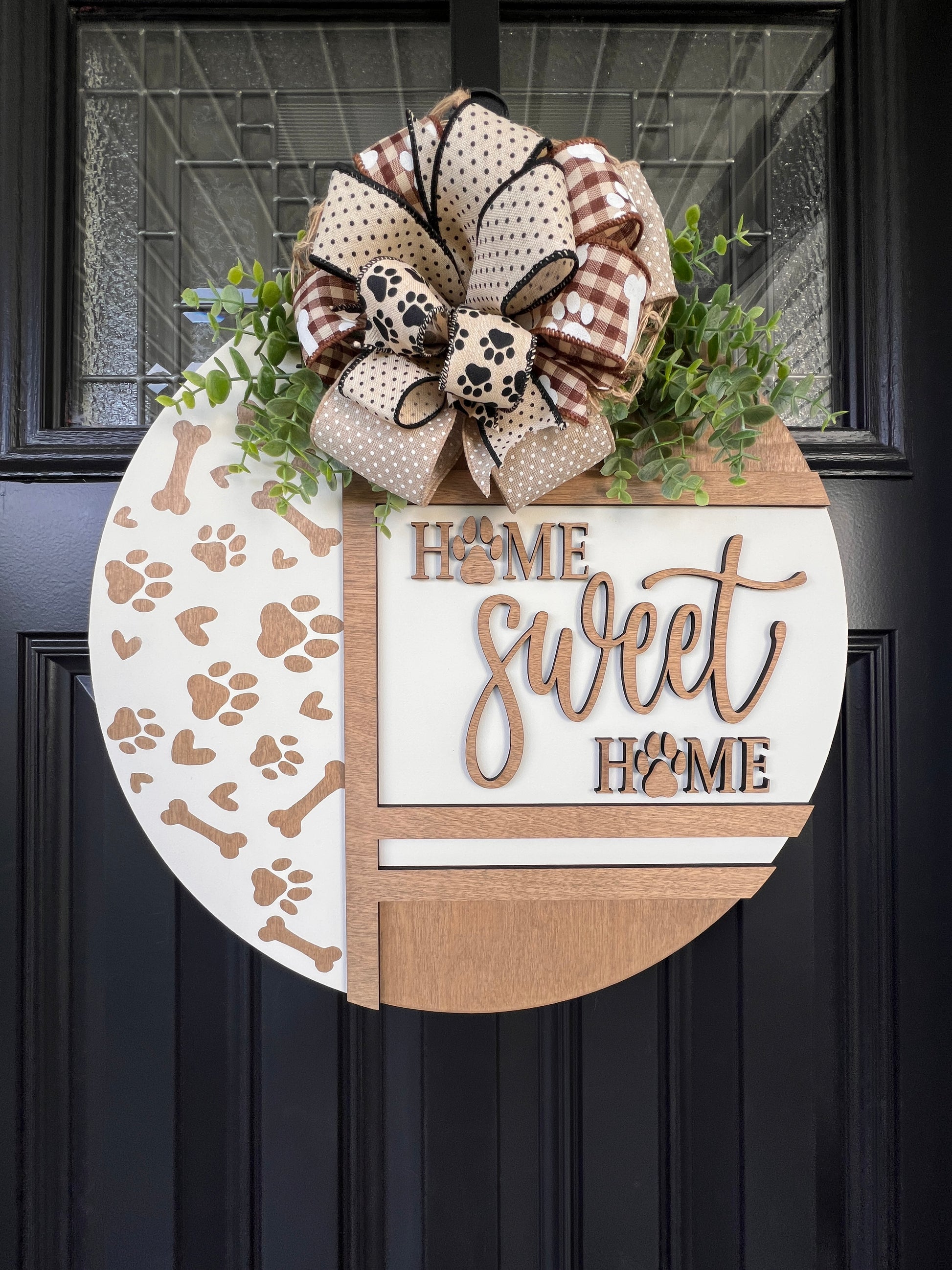 Handmade Home Sweet Home dog lover door hanger featuring laser-cut paw prints, dog bone accents, stained birchwood details, greenery, and a coordinating designer bow. 