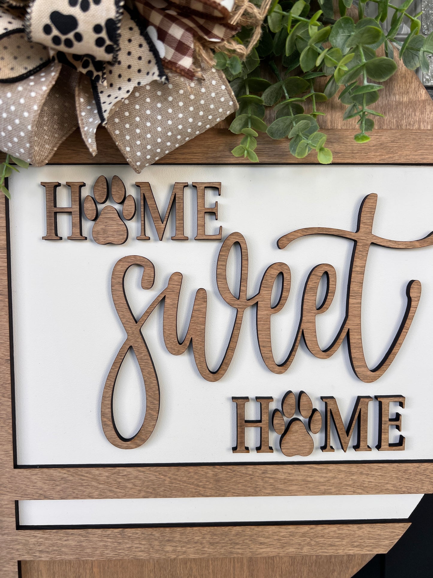 Handmade Home Sweet Home dog lover door hanger featuring laser-cut paw prints, dog bone accents, stained birchwood details, greenery, and a coordinating designer bow. 