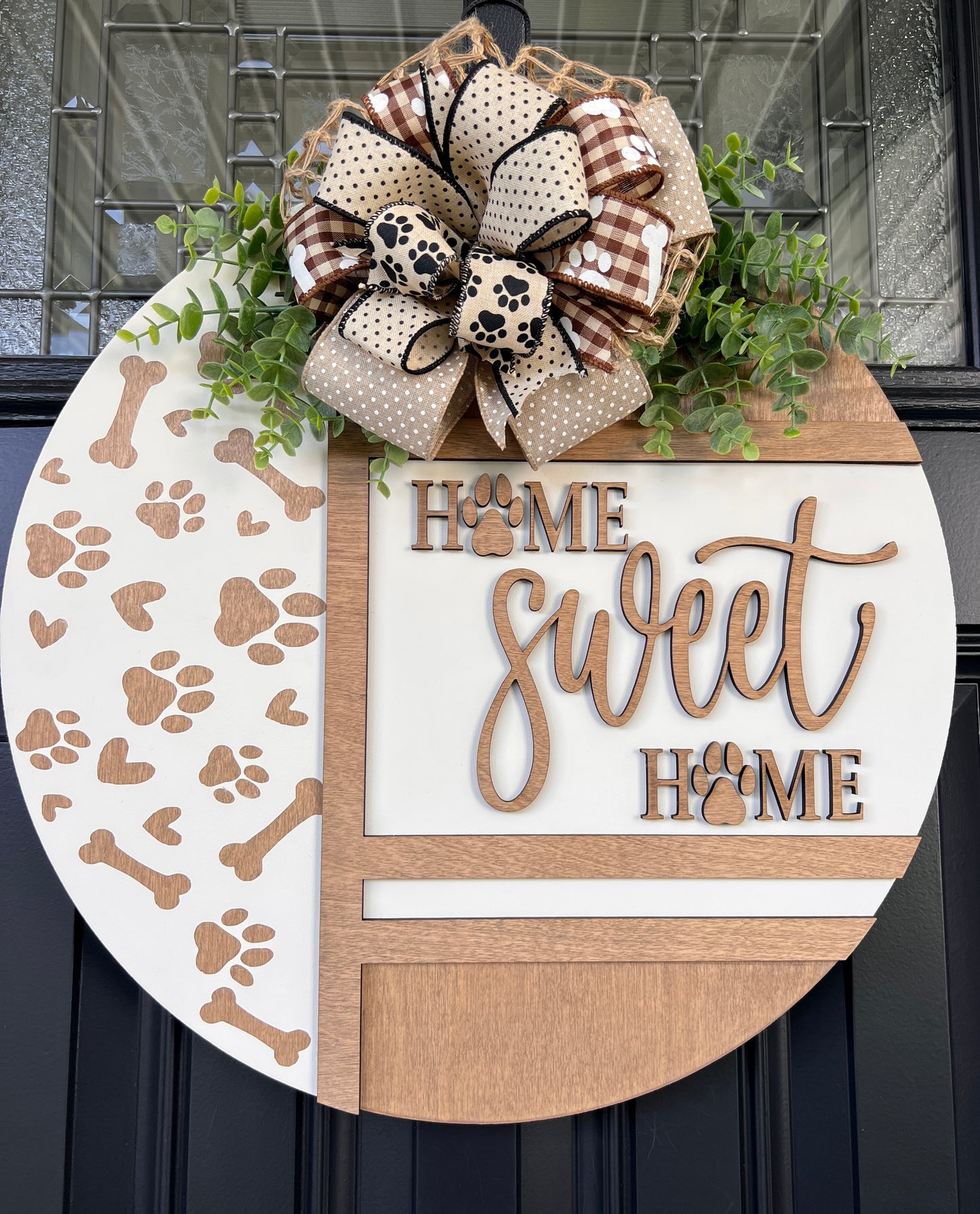 Handmade Home Sweet Home dog lover door hanger featuring laser-cut paw prints, dog bone accents, stained birchwood details, greenery, and a coordinating designer bow. 