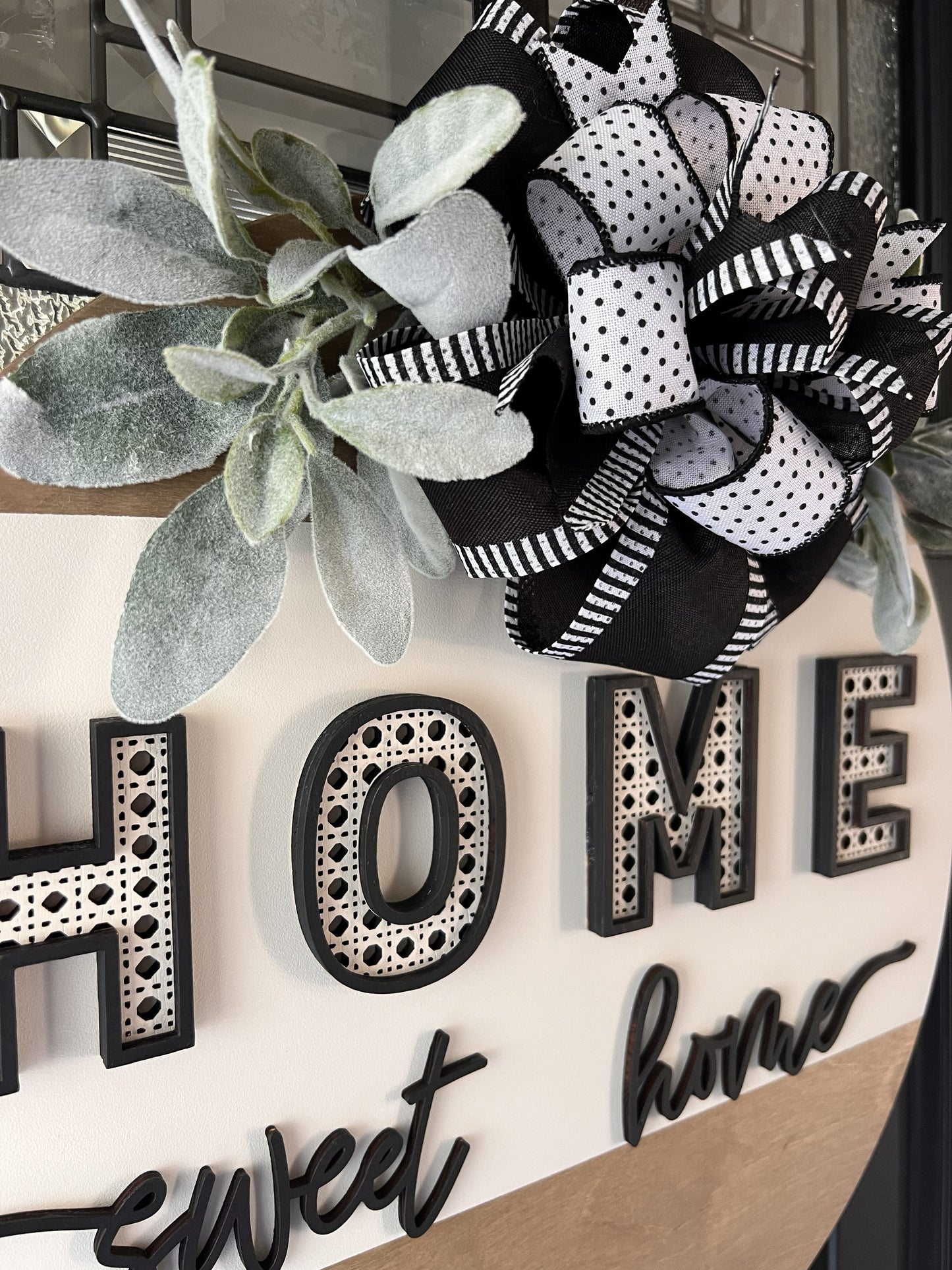 “Home Sweet Home black and white wooden door hanger with layered lettering, decorative bow and greenery on front door”