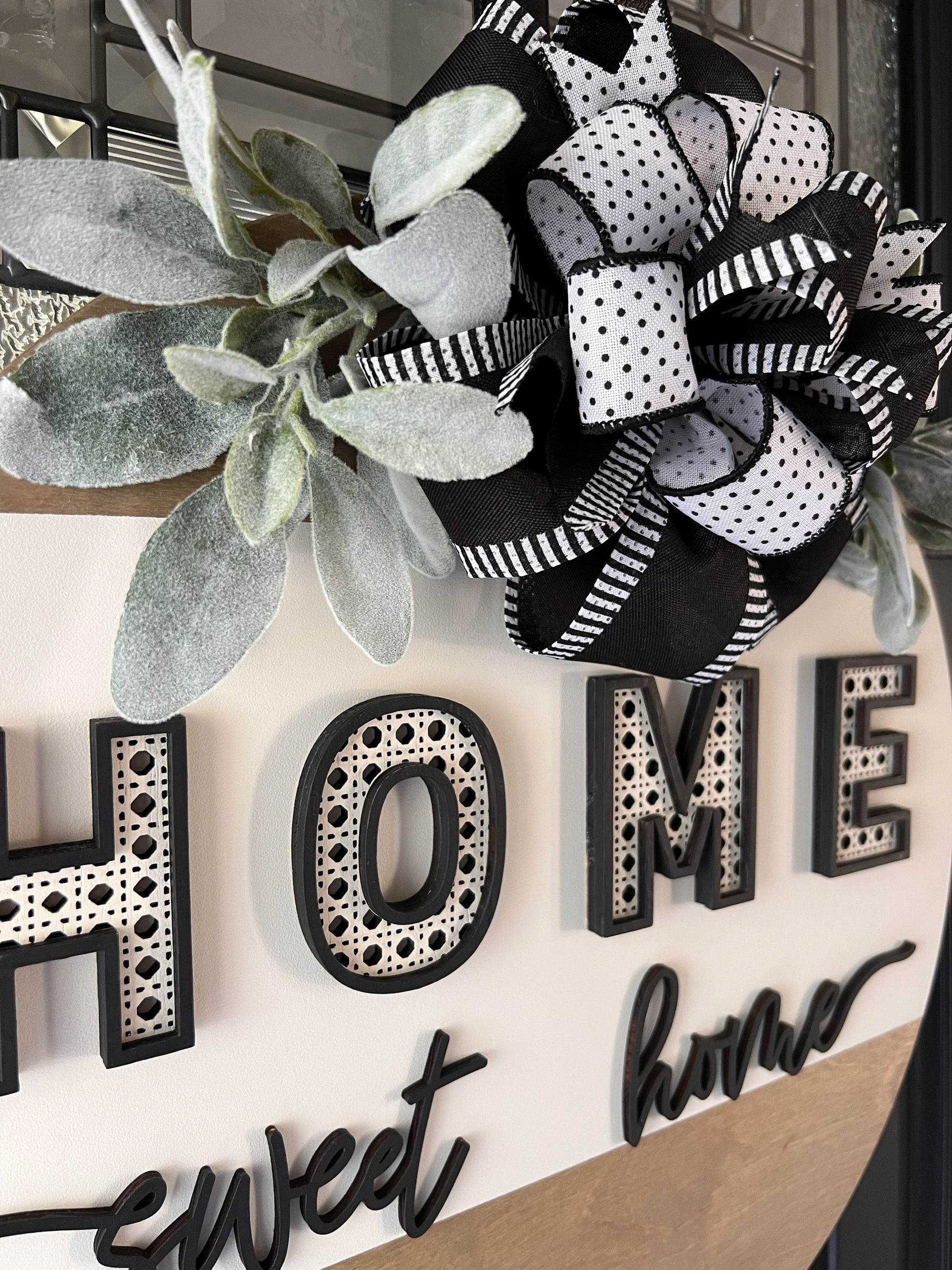 “Home Sweet Home black and white wooden door hanger with layered lettering, decorative bow and greenery on front door”