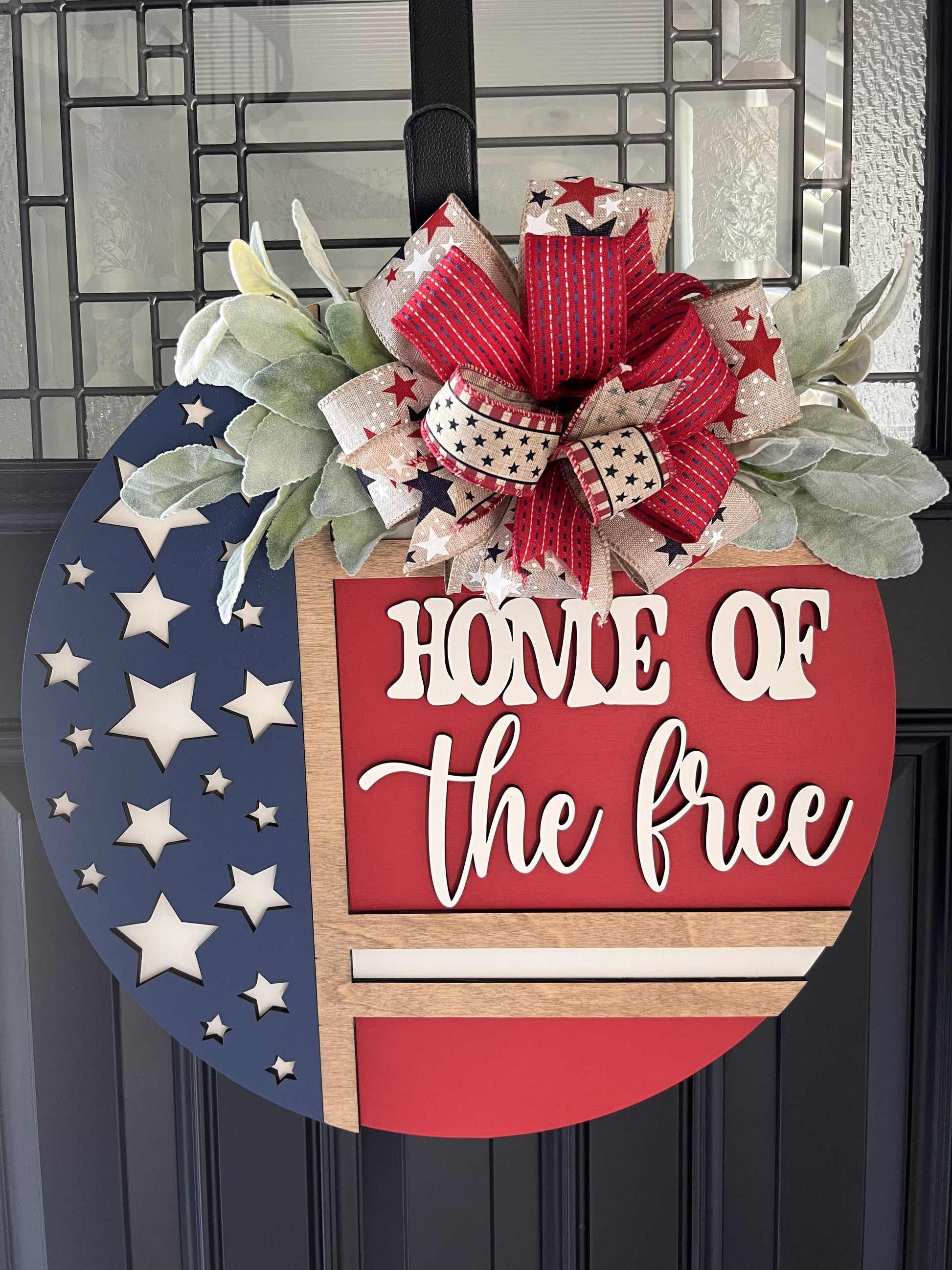 Decorative door hanger with 'Home of the Free' text and American flag design.