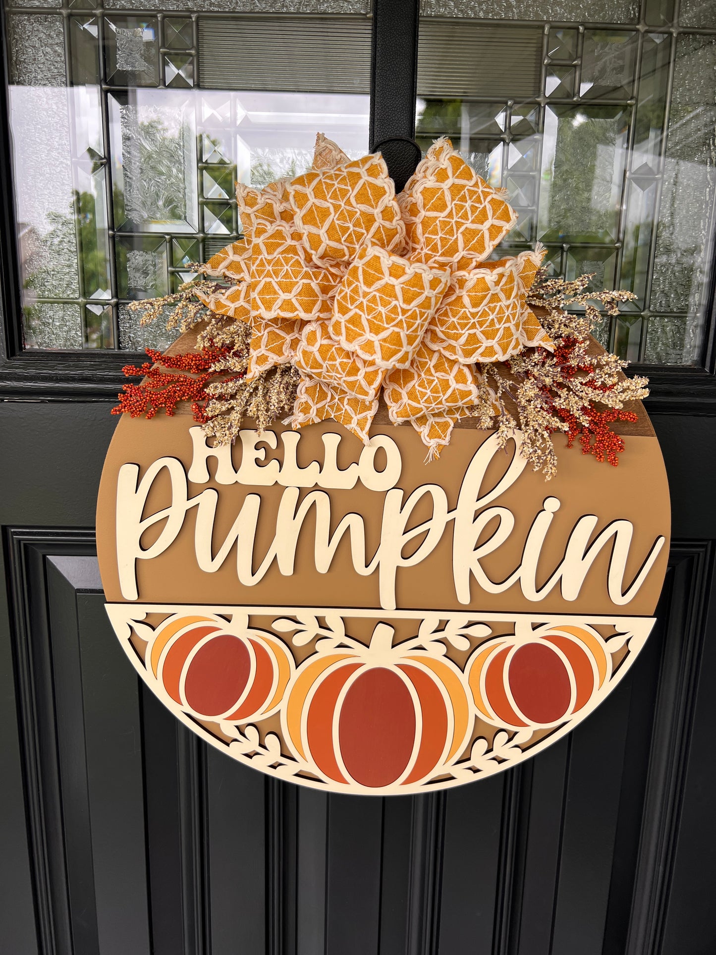 Hello Pumpkin Trio door hanger full view on black door showing warm caramel background with 3D cream lettering and oversized bow