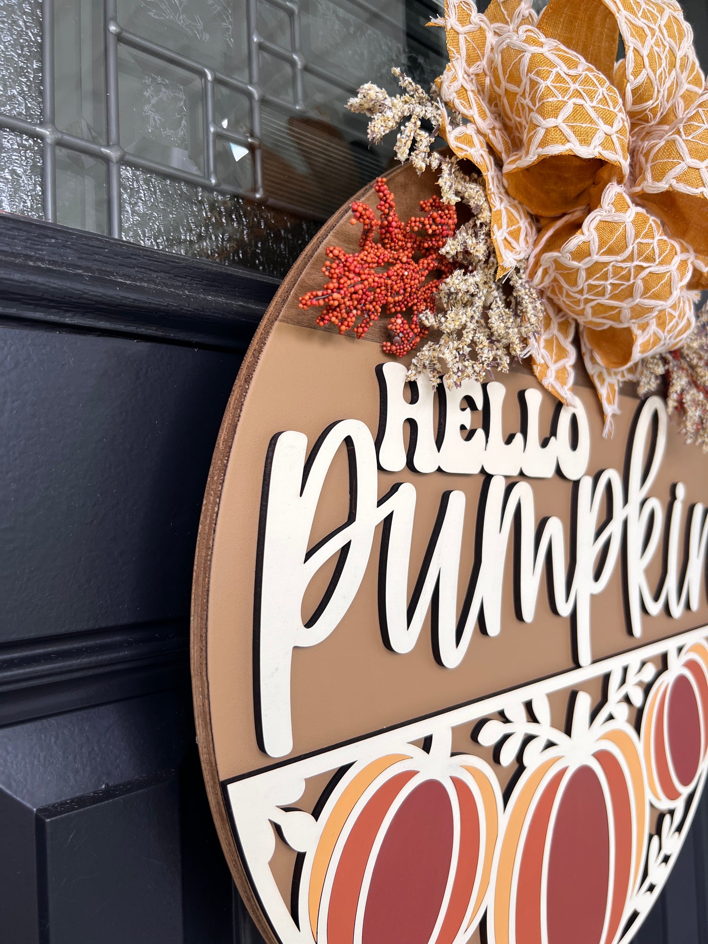 Hello Pumpkin Trio door hanger angled close up showing depth of 3D cream lettering and red berry spray detail against caramel background