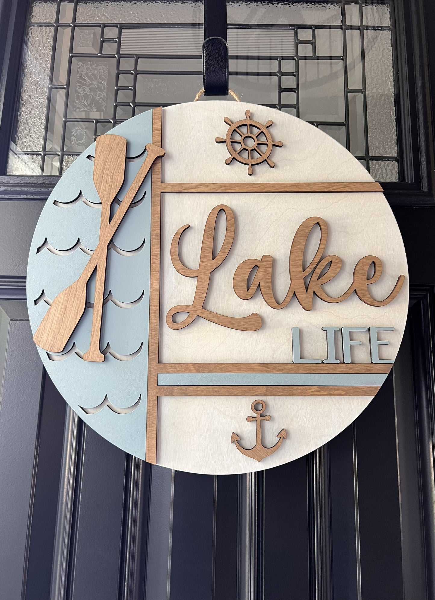 Decorative sign with 'Lake Life' text, paddle, wheel, and anchor on a circular background.
