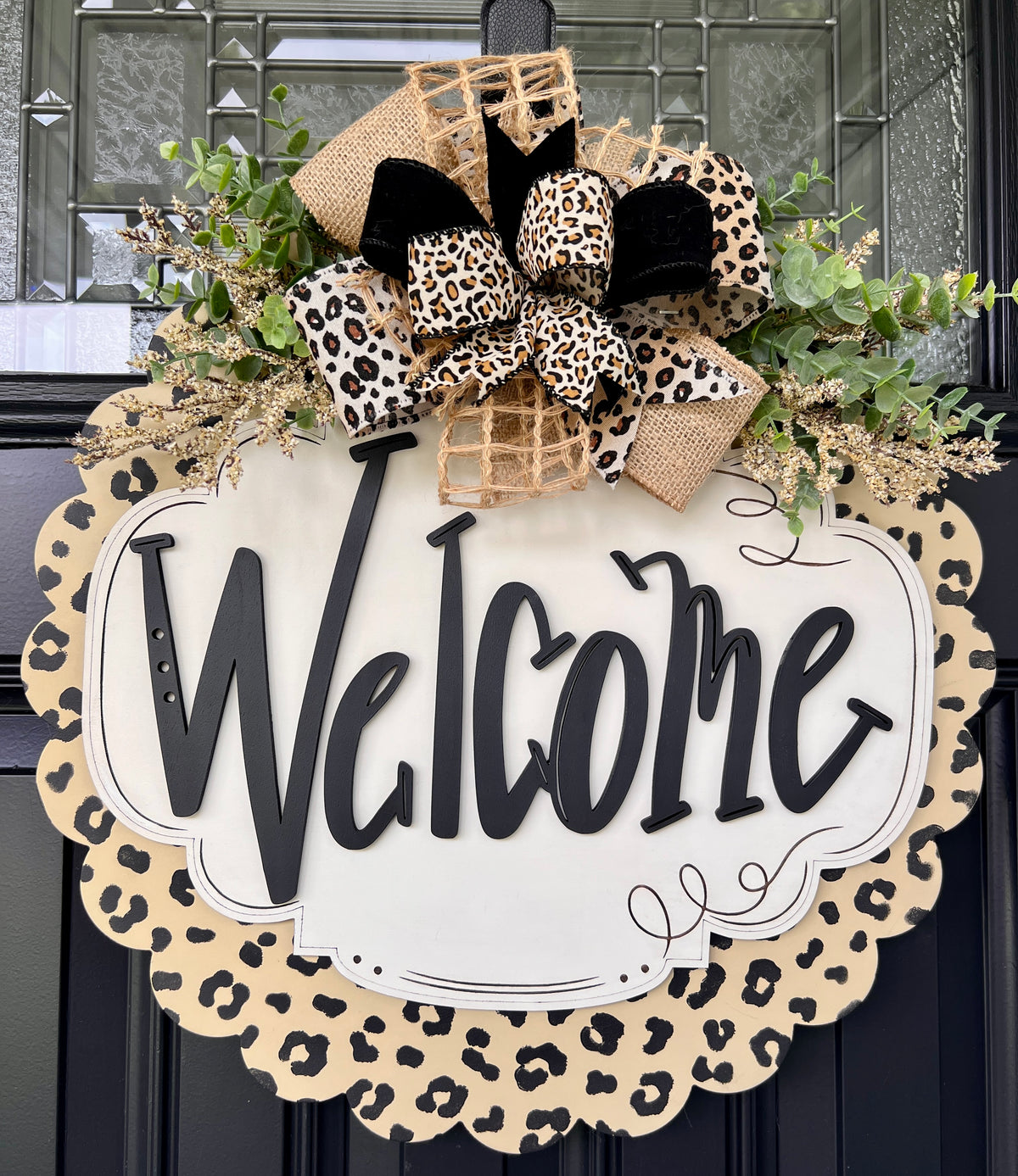 Angled view of leopard print Welcome door hanger with black door background