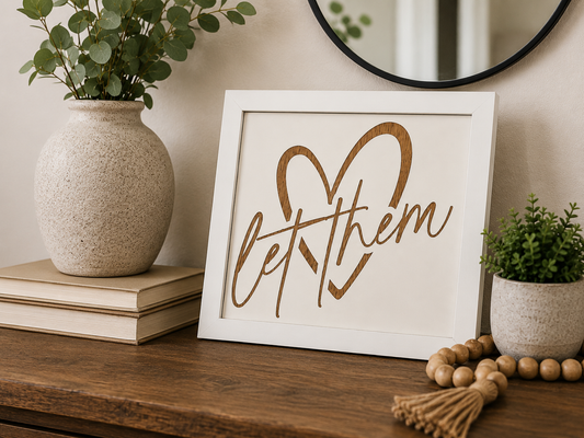 Let Them engraved birch wood sign with heart design in white frame, styled on a wood console table with greenery and beaded garland