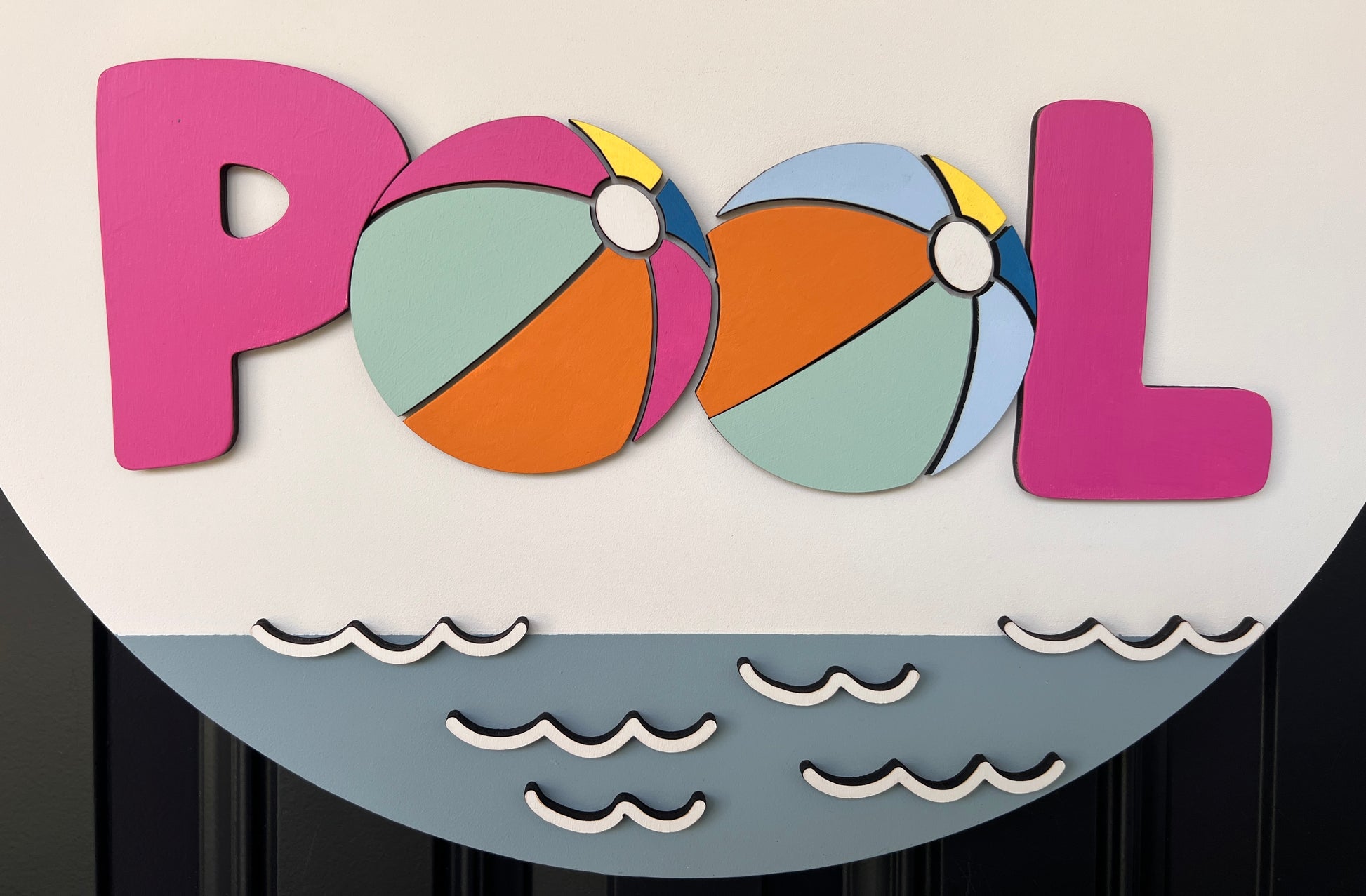 Handcrafted round door hanger featuring the phrase "Life Is Better at the Pool" with colorful beach ball accents, summer colors, and a bright pink and blue designer bow displayed on a front door.